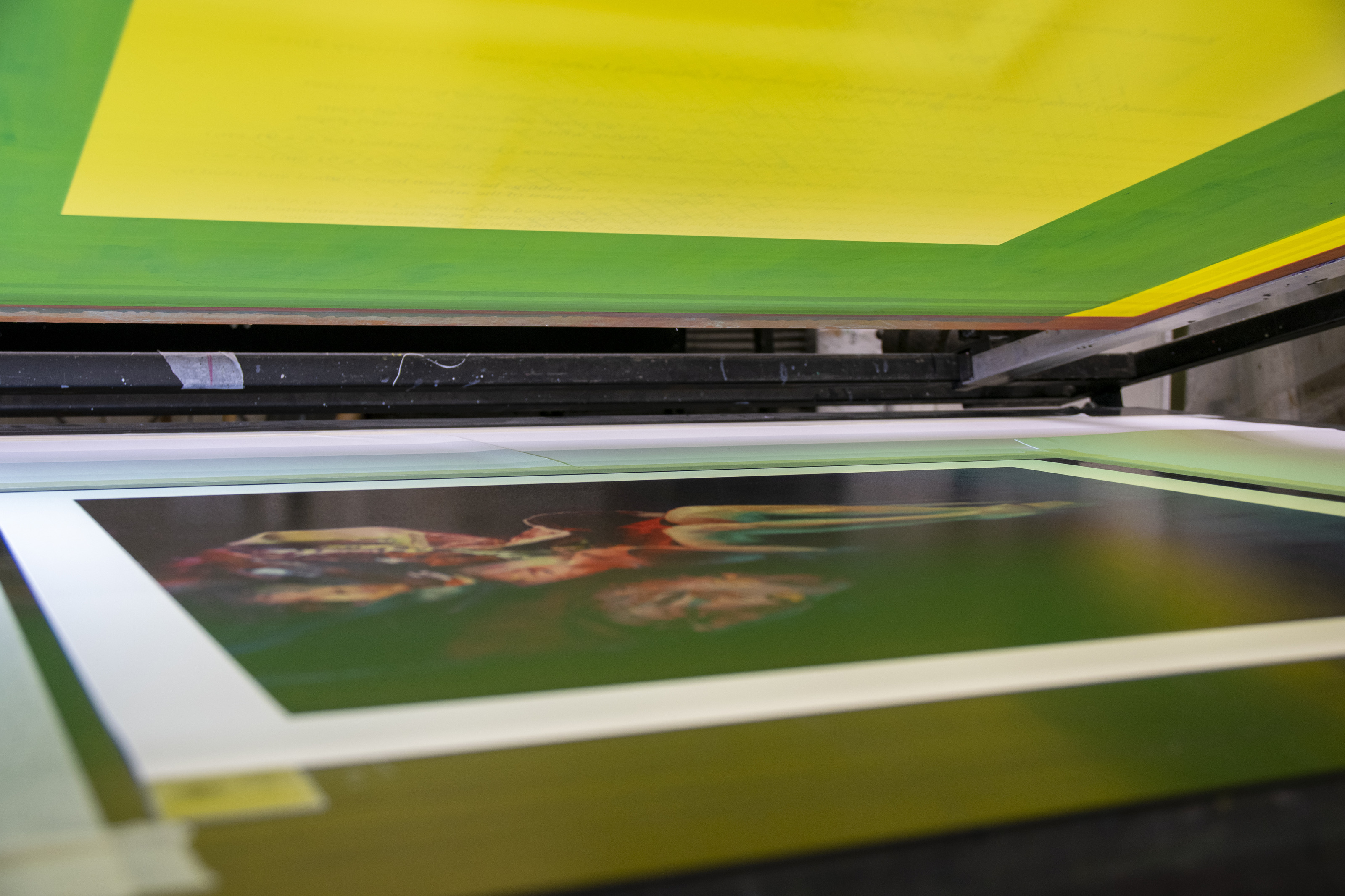 A Chloe Early print on the press bed at Atelier JI, a raised yellow-and-green screen lifted above the colour-saturated sheet.