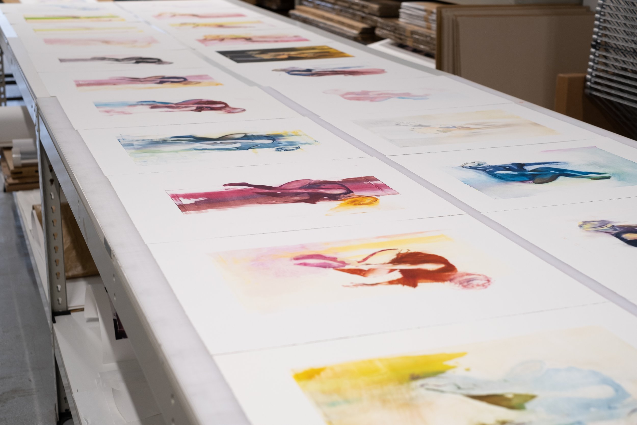 Rows of Chloe Early's unique oil monotypes laid out on a studio table at Atelier JI, each a different figure in saturated colour.