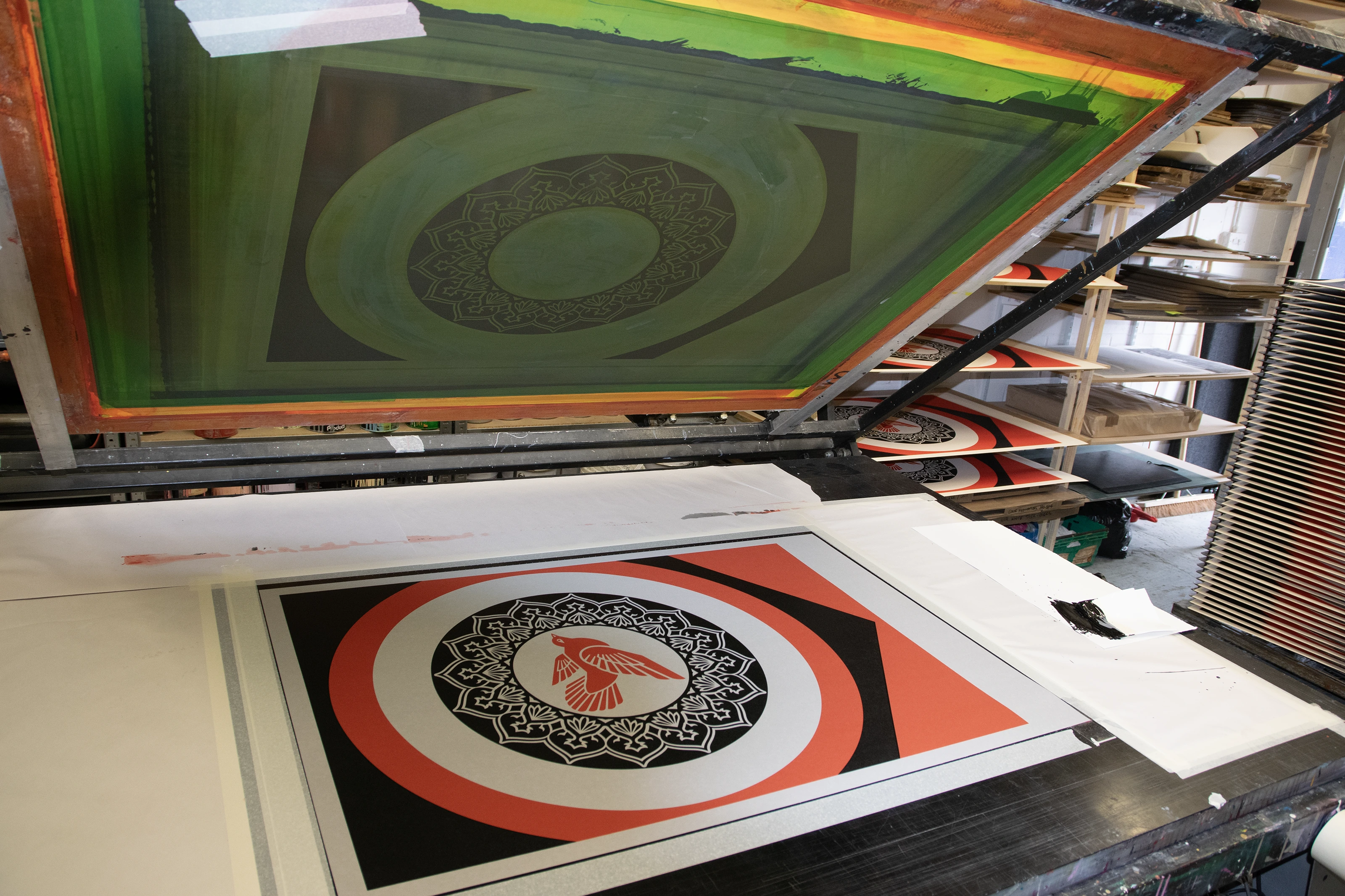 A raised silkscreen above a freshly pulled Rise from the Ashes print at Atelier JI, more prints drying on racks behind.