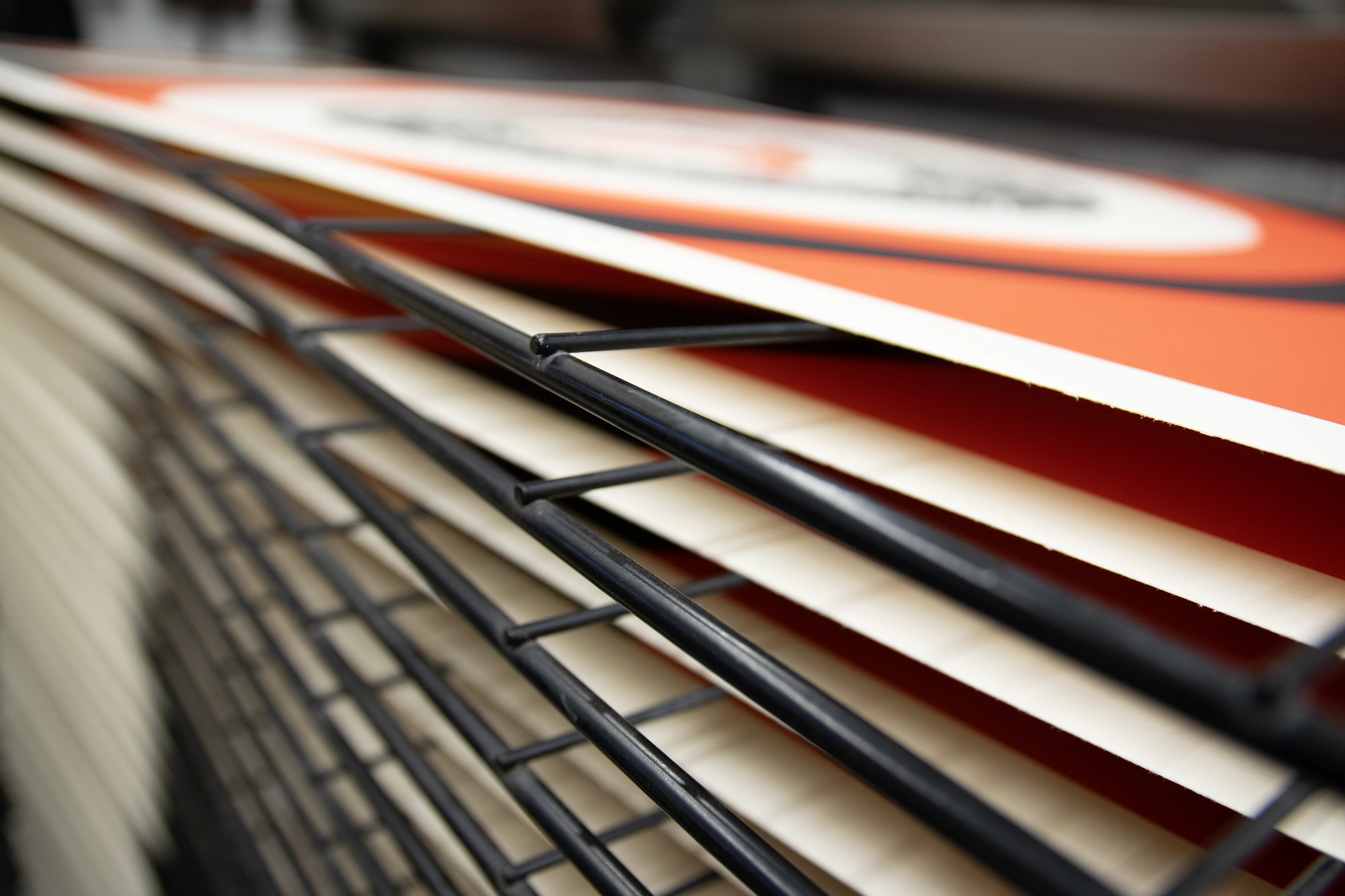 Freshly printed Rise from the Ashes editions drying on a studio rack at Atelier JI, red-orange and cream edges stacked in rows.
