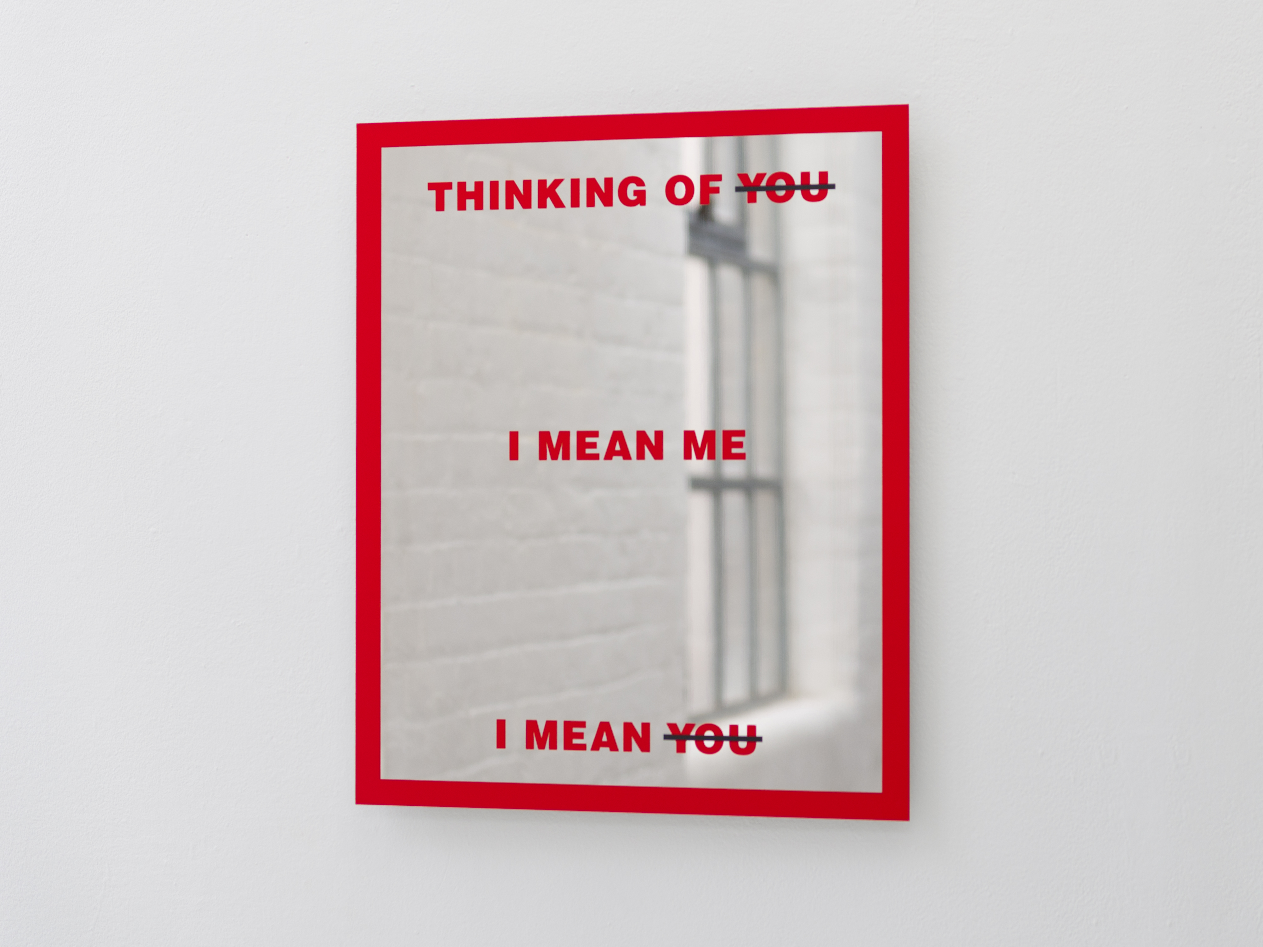 Barbara Kruger's Untitled (Mirror) on a white gallery wall, its mirrored surface reflecting a barred window and brickwork behind the red text.