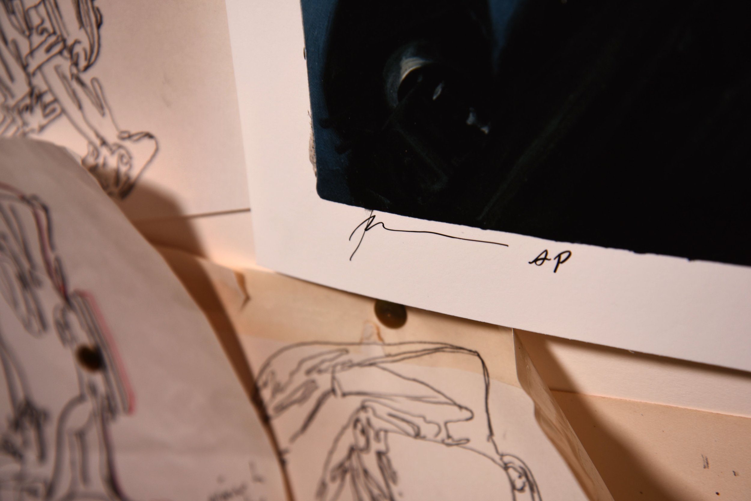 Detail of a signed Phil Hale print marked 'AP', pinned among loose pen studies of figures in his studio.