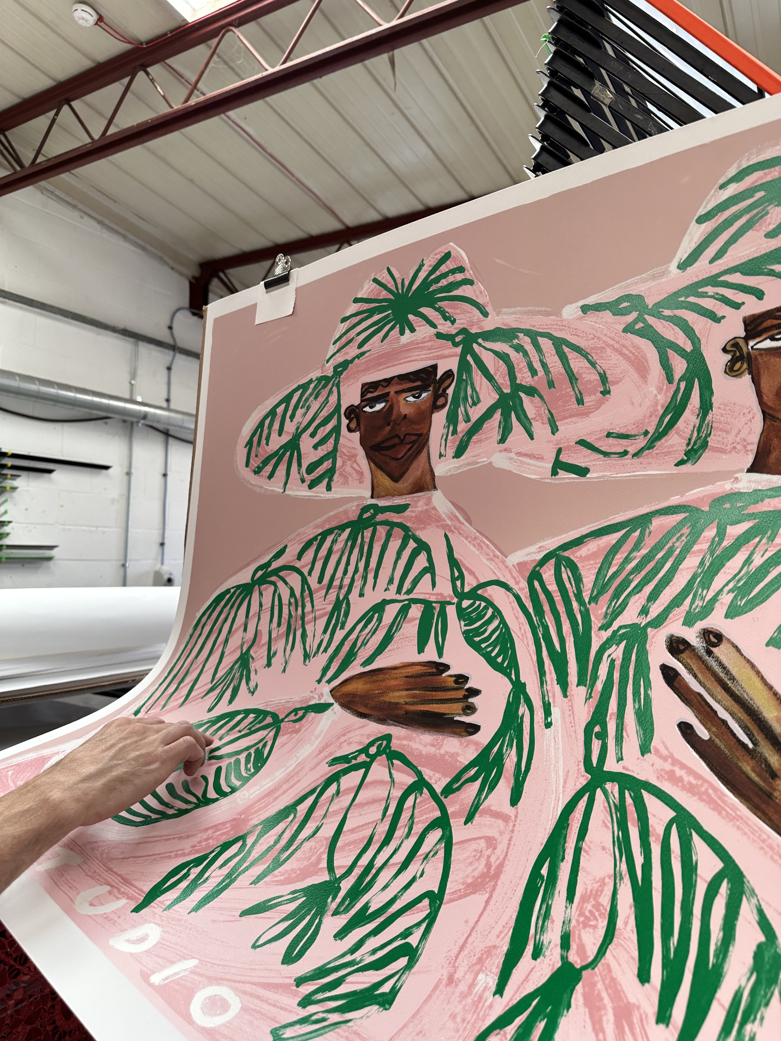 A large Lora print by Studio Lenca clipped up at the Atelier JI studio, its pink and green figures drying, a hand steadying it.