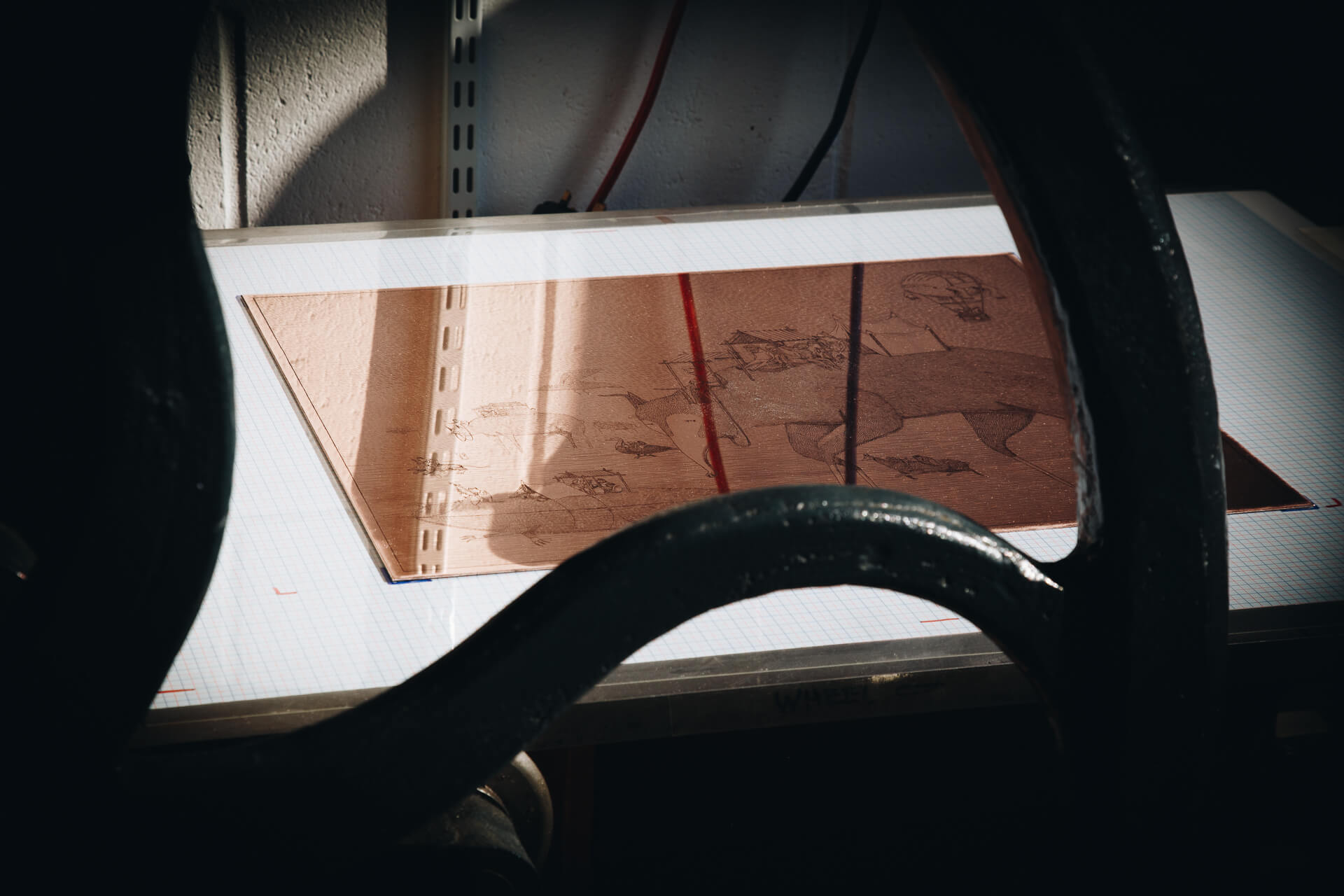 The etched copper Migration plate on the press bed at the Atelier JI studio, its fine-line scene catching the light.