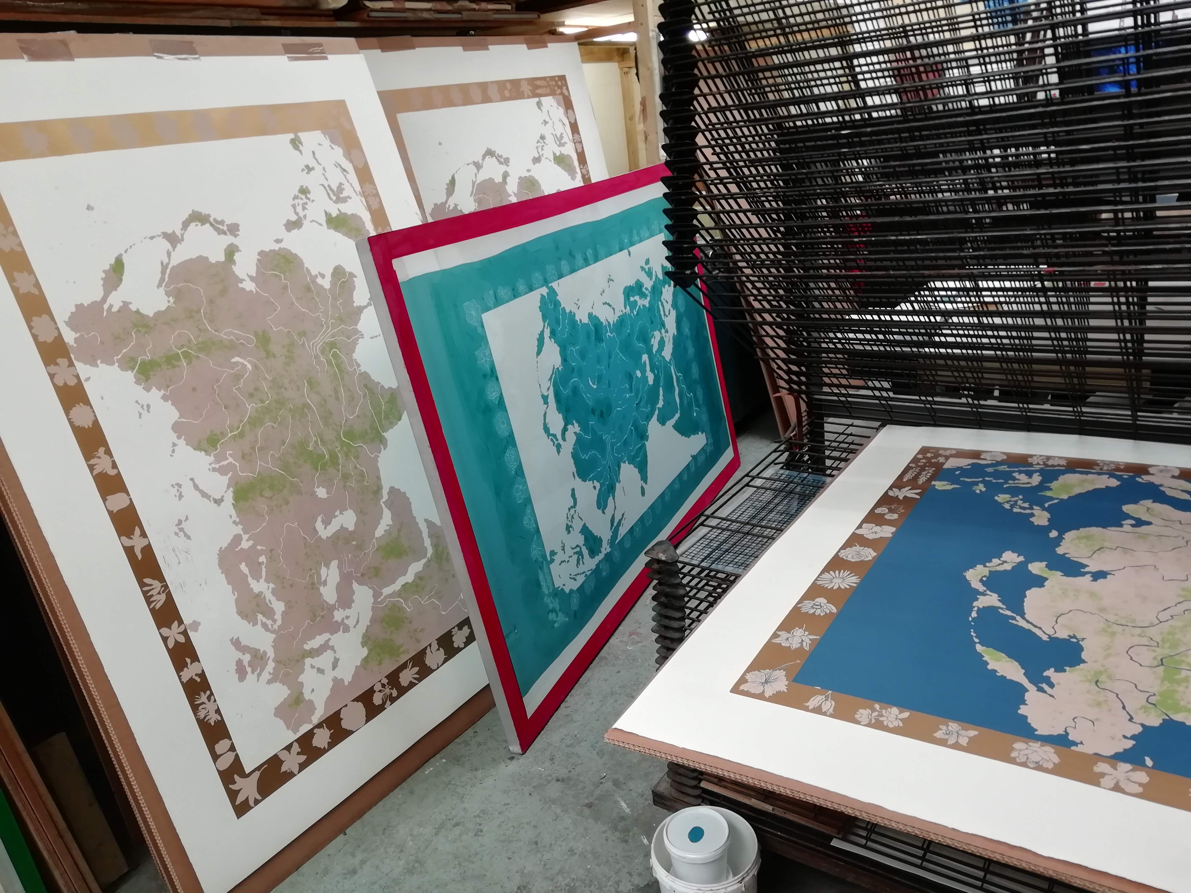 The Silk Road in production: partly printed colour states of Barratt's map drying on studio racks beside a screen.