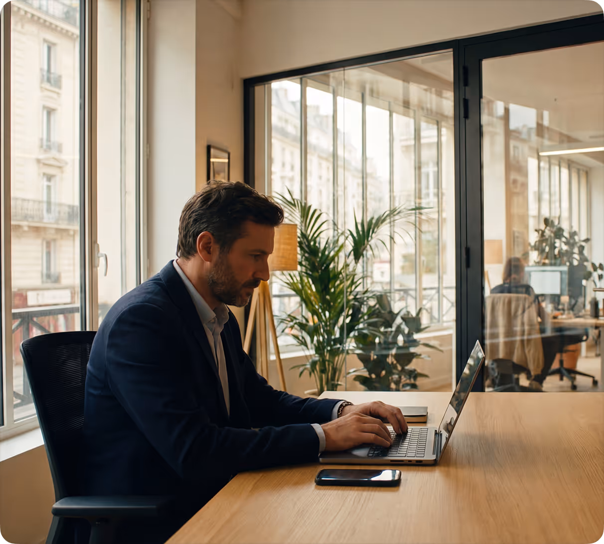 Homme d'affaires travaillant sur un ordinateur portable à un bureau moderne avec une fenêtre donnant sur la ville.