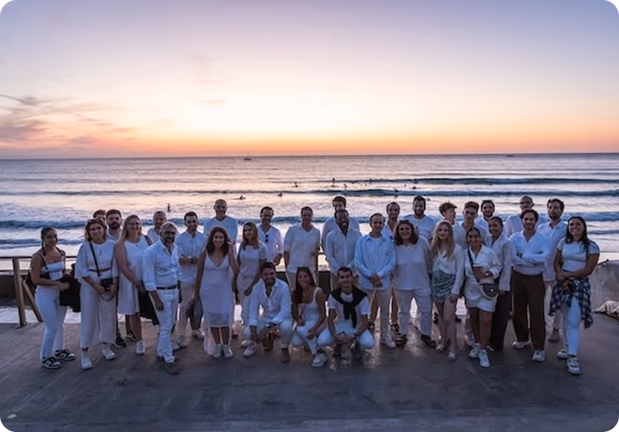 Groupe de personnes vêtues de blanc posant sur une plage au coucher du soleil.