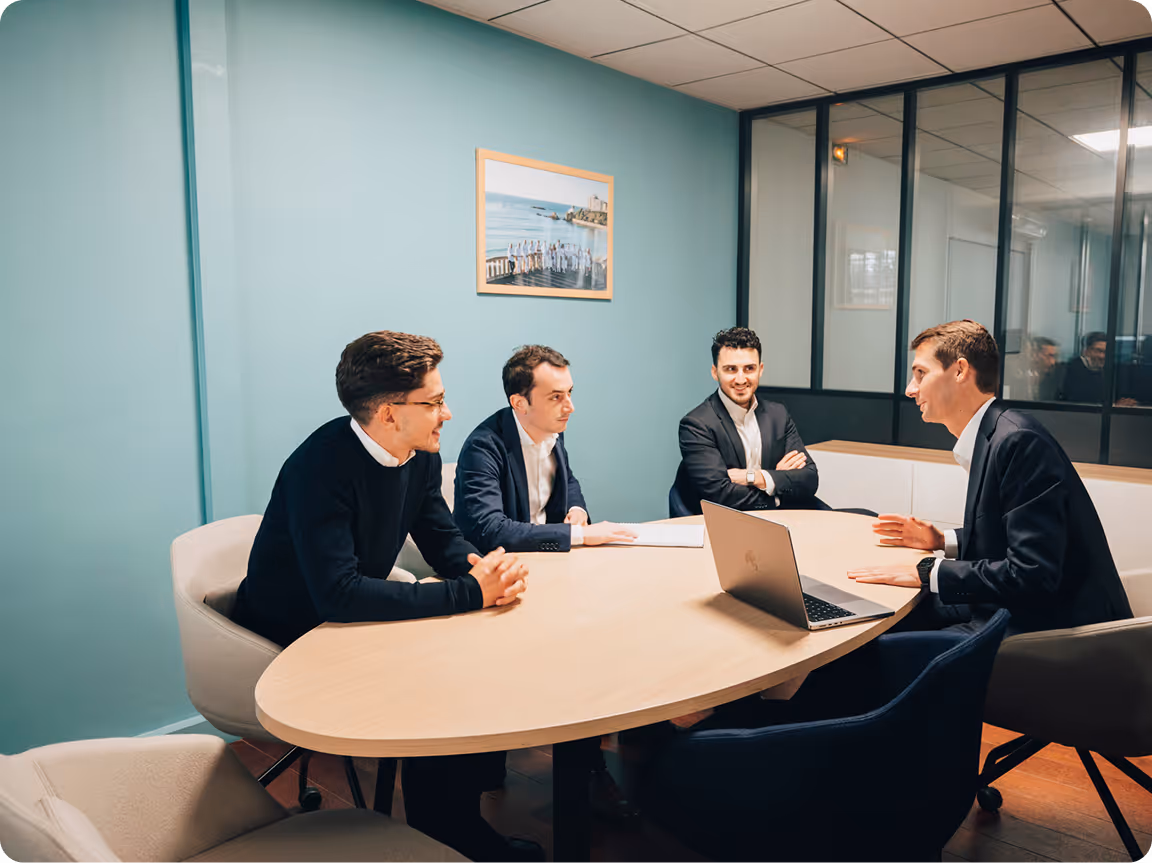 Quatre hommes en réunion d'affaires autour d'une table avec un ordinateur portable dans une salle moderne.