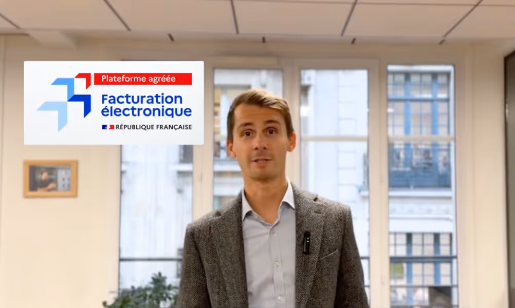 Un homme en veste grise parle devant une fenêtre avec le logo Facturation électronique France.