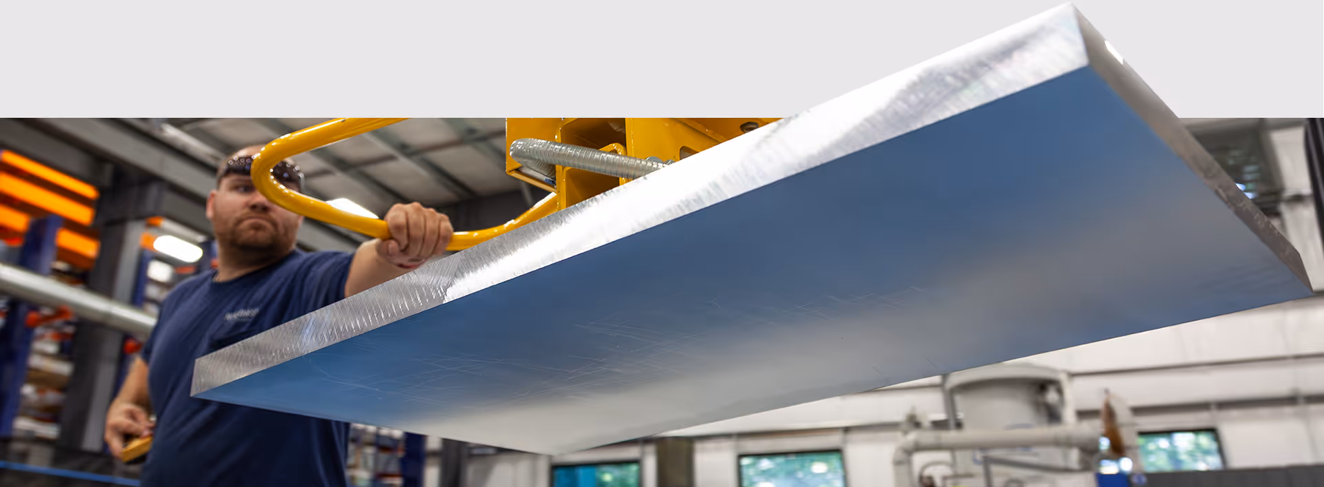 Industrial worker handling precision aluminum plate material inside a metal processing and manufacturing facility