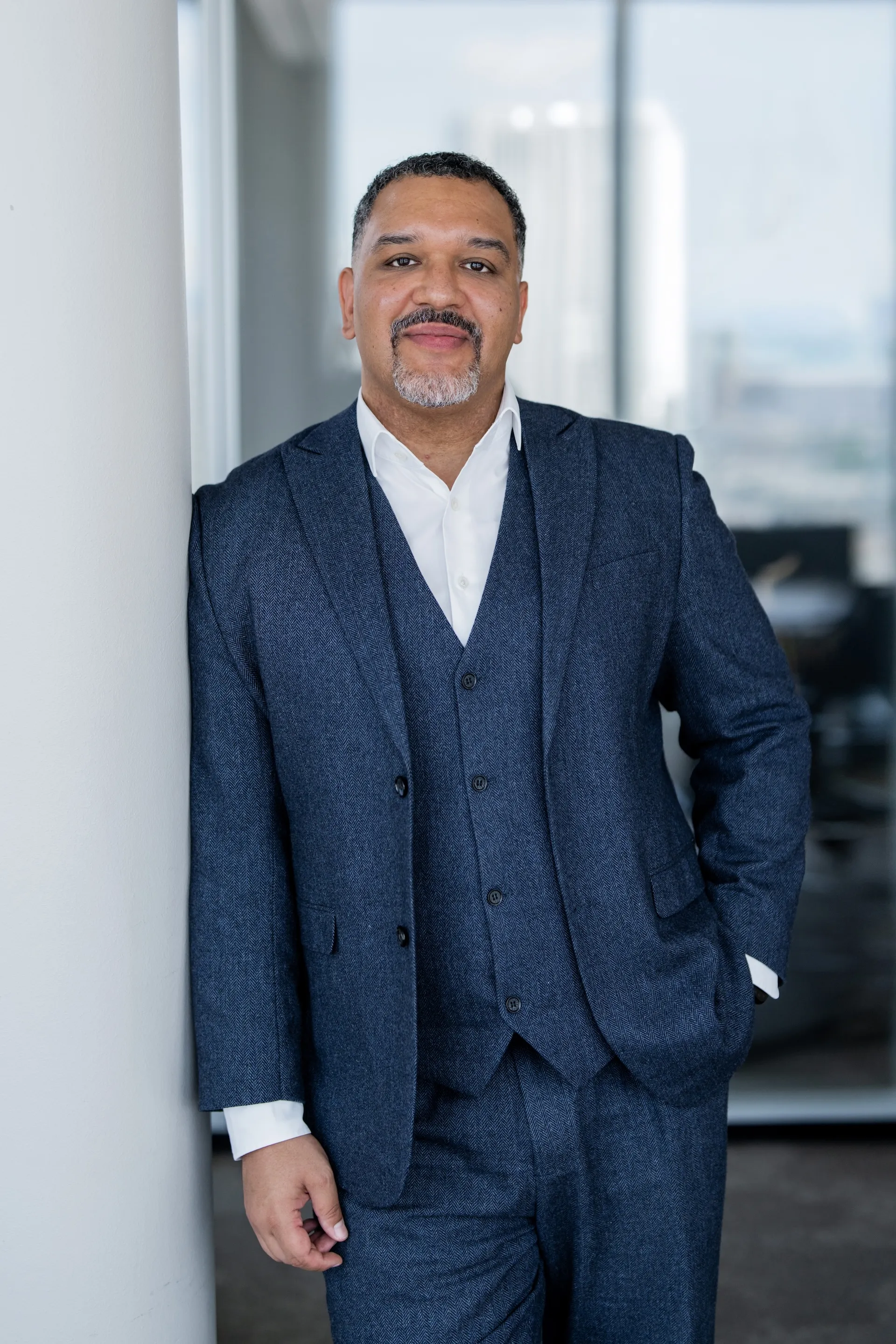Fabio Waldrón Pelegrin lehnt lächelnd an weißer Säule, trägt dunklen Anzug und weißes Hemd in Büroumgebung.