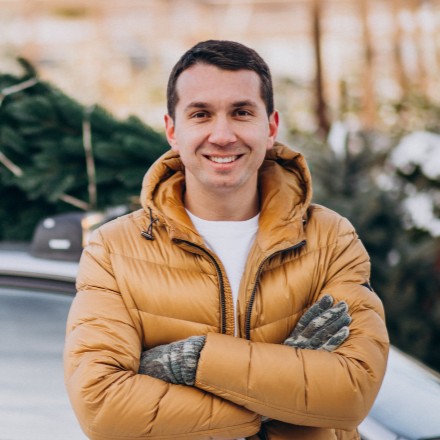 Poträt eines Fahrlehrers mit verschränkten Armen vor seinem Auto