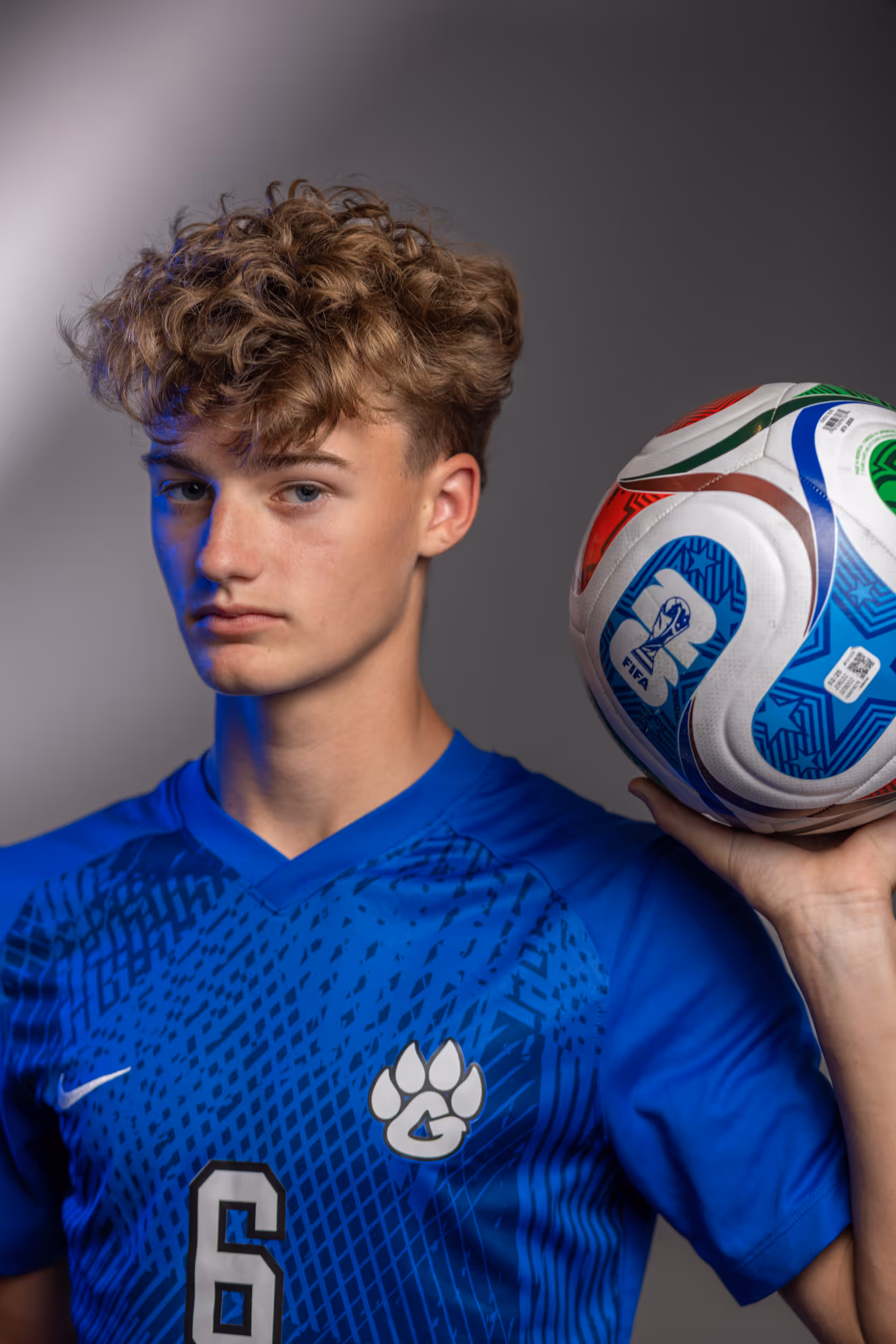 Weston Ochs in blue soccer jersey holding a FIFA World Cup soccer ball on shoulder.