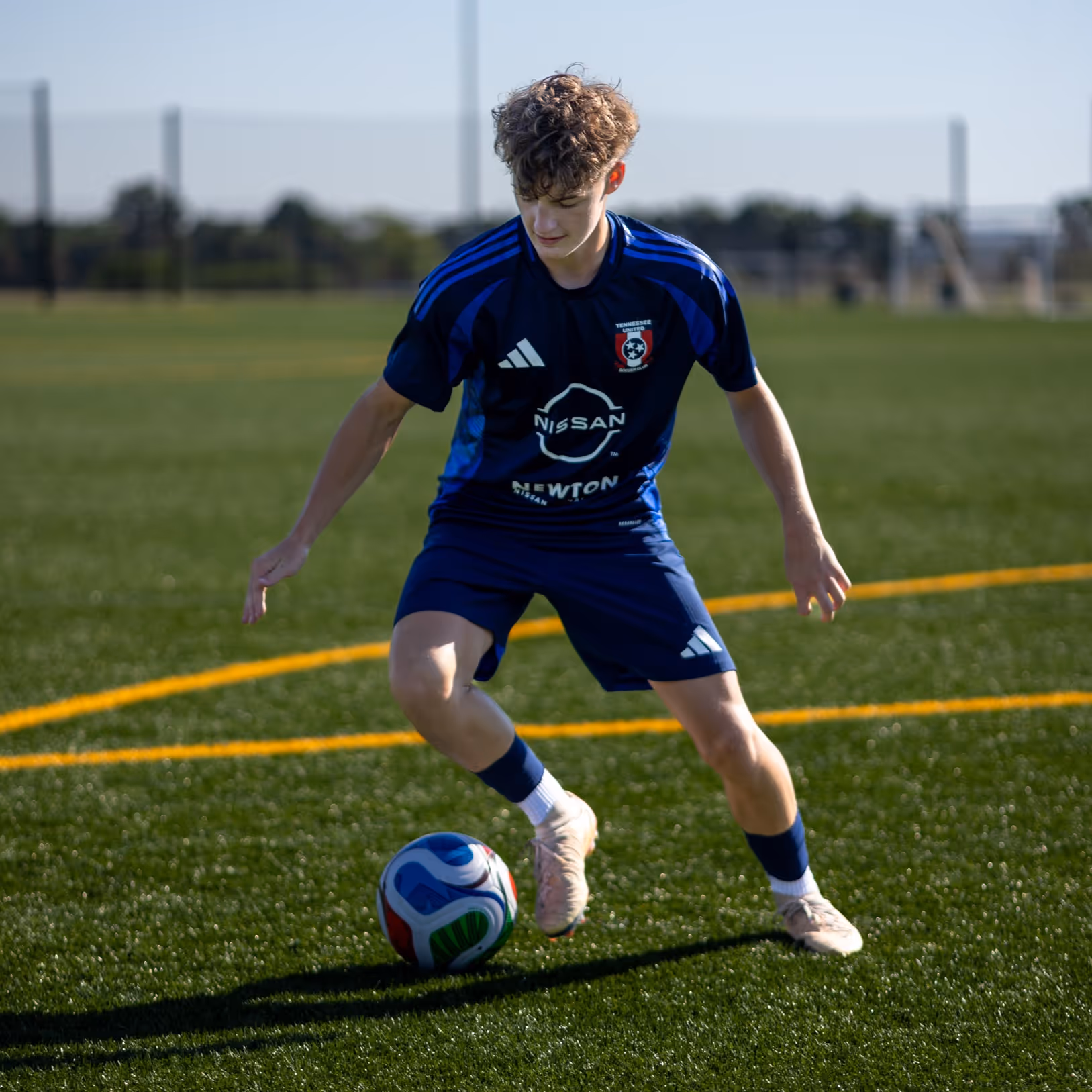 Weston Ochs in blue uniform controlling a colorful soccer ball on grass field.