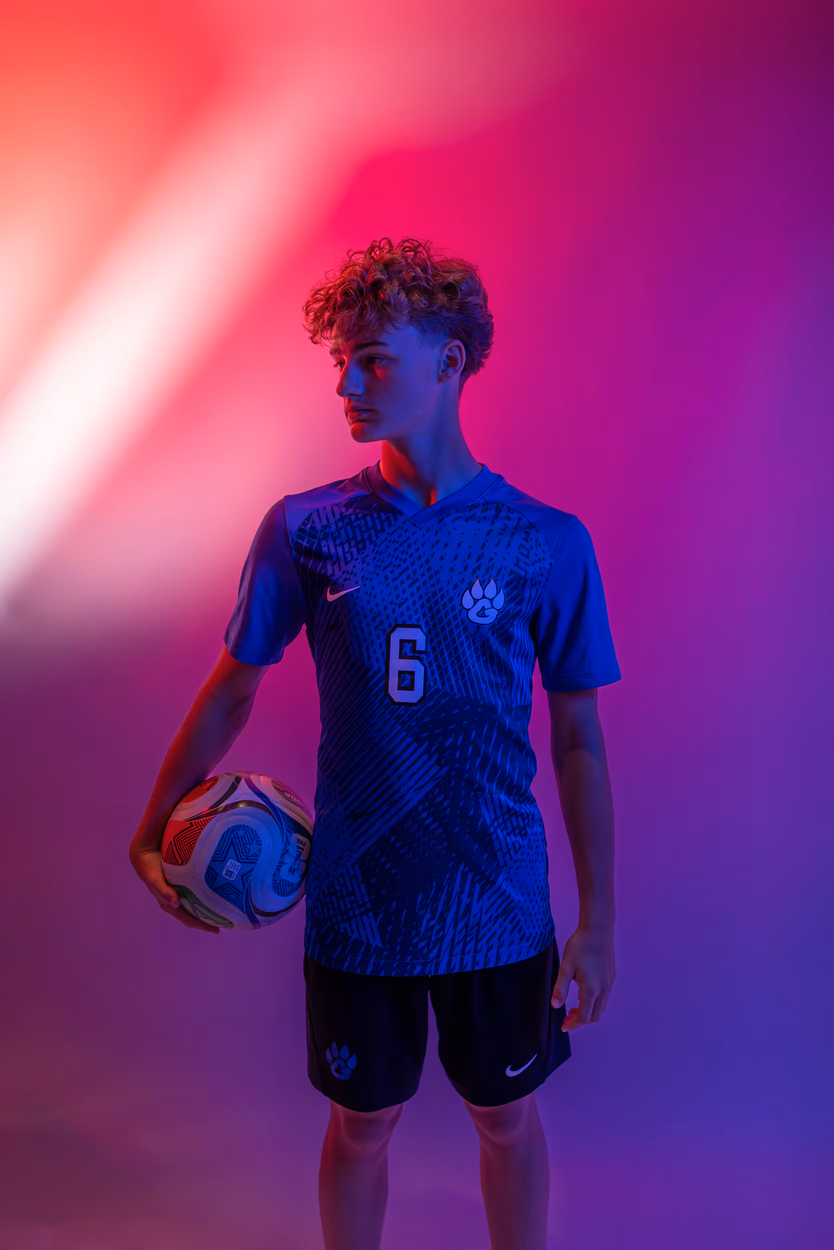 Weston Ochs holding a soccer ball against pink and purple light backdrop.