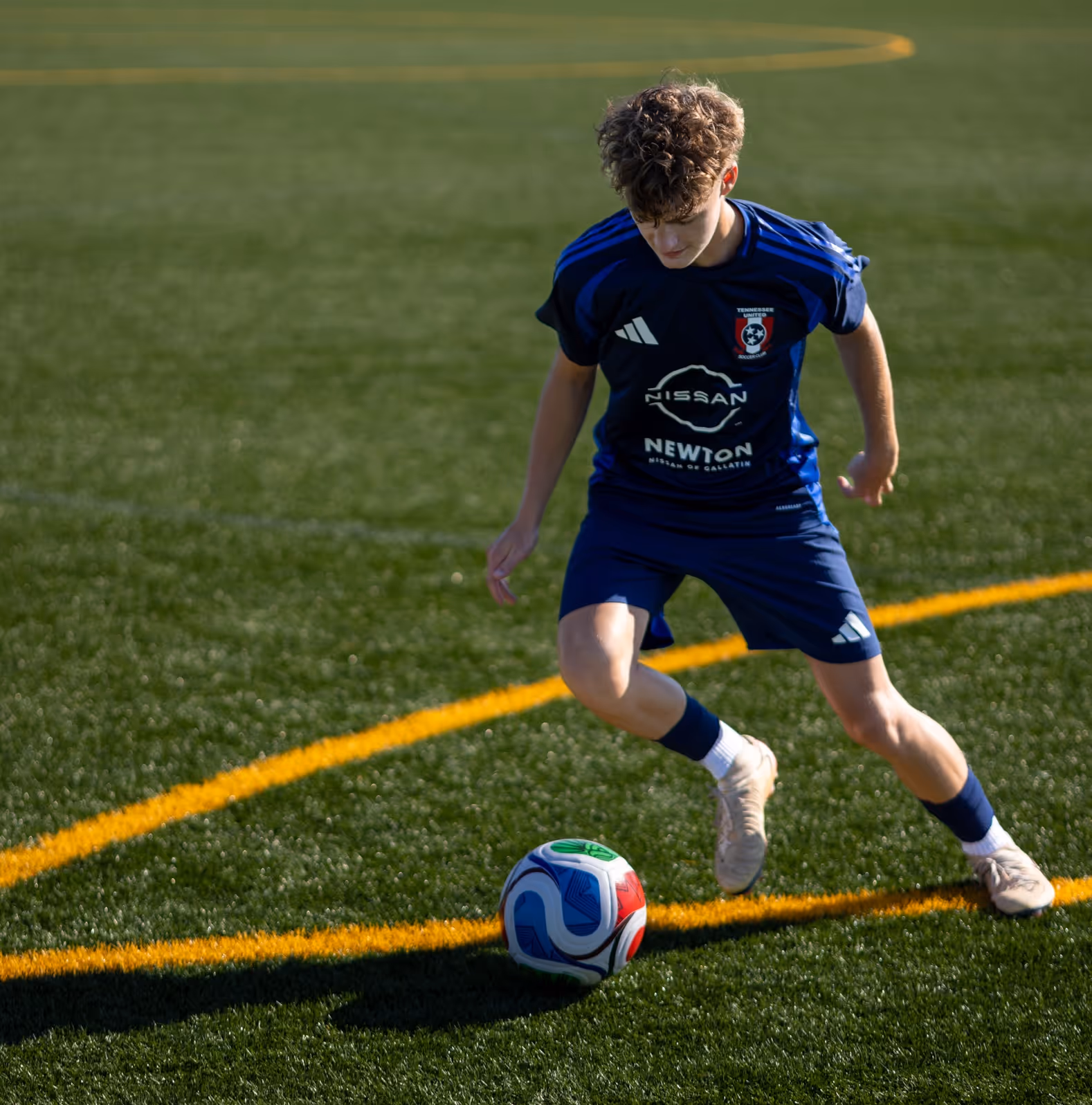 Weston Ochs in blue dribbling a colorful ball on a green field with orange lines.