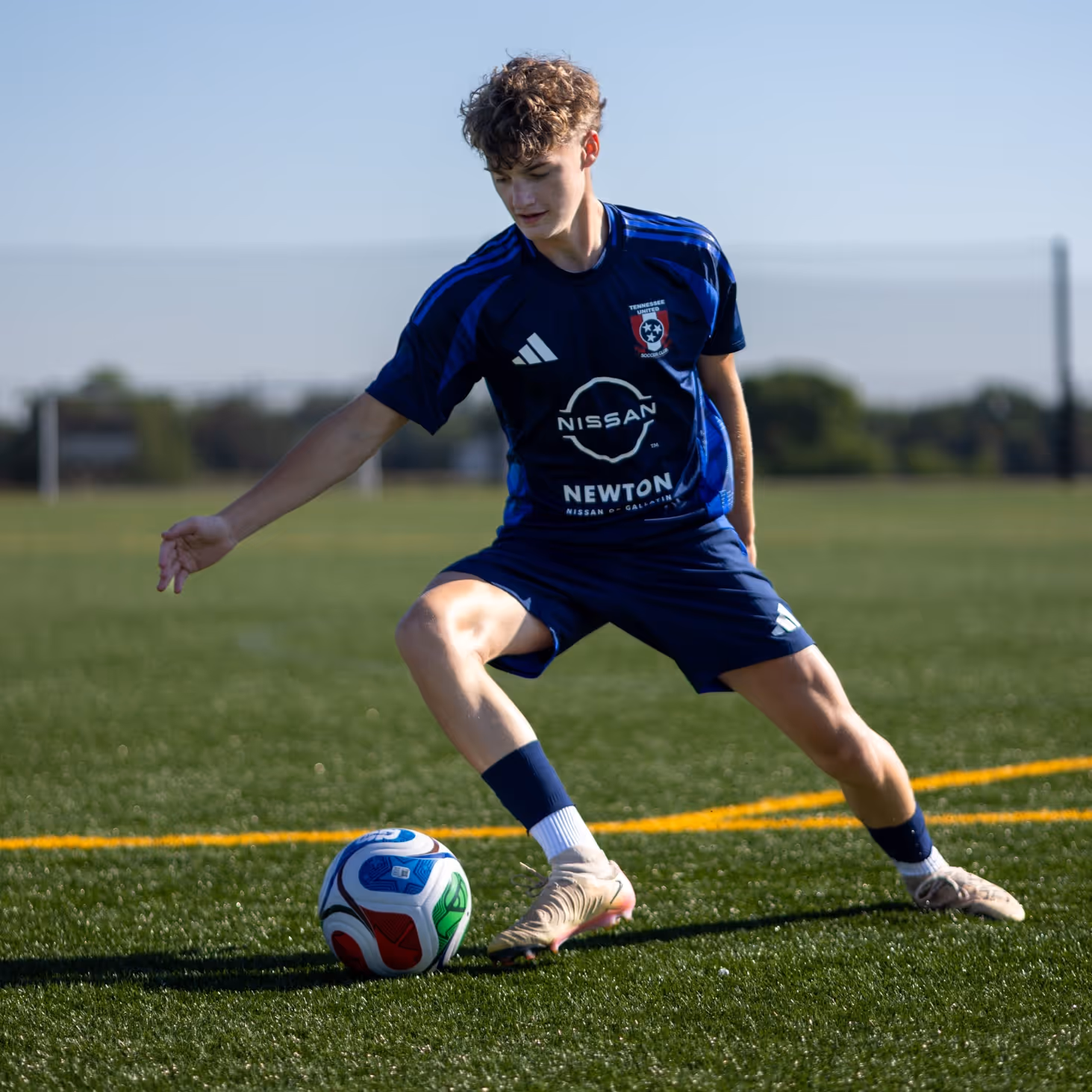 Weston Ochs in blue uniform controlling a ball on a green field under clear sky.