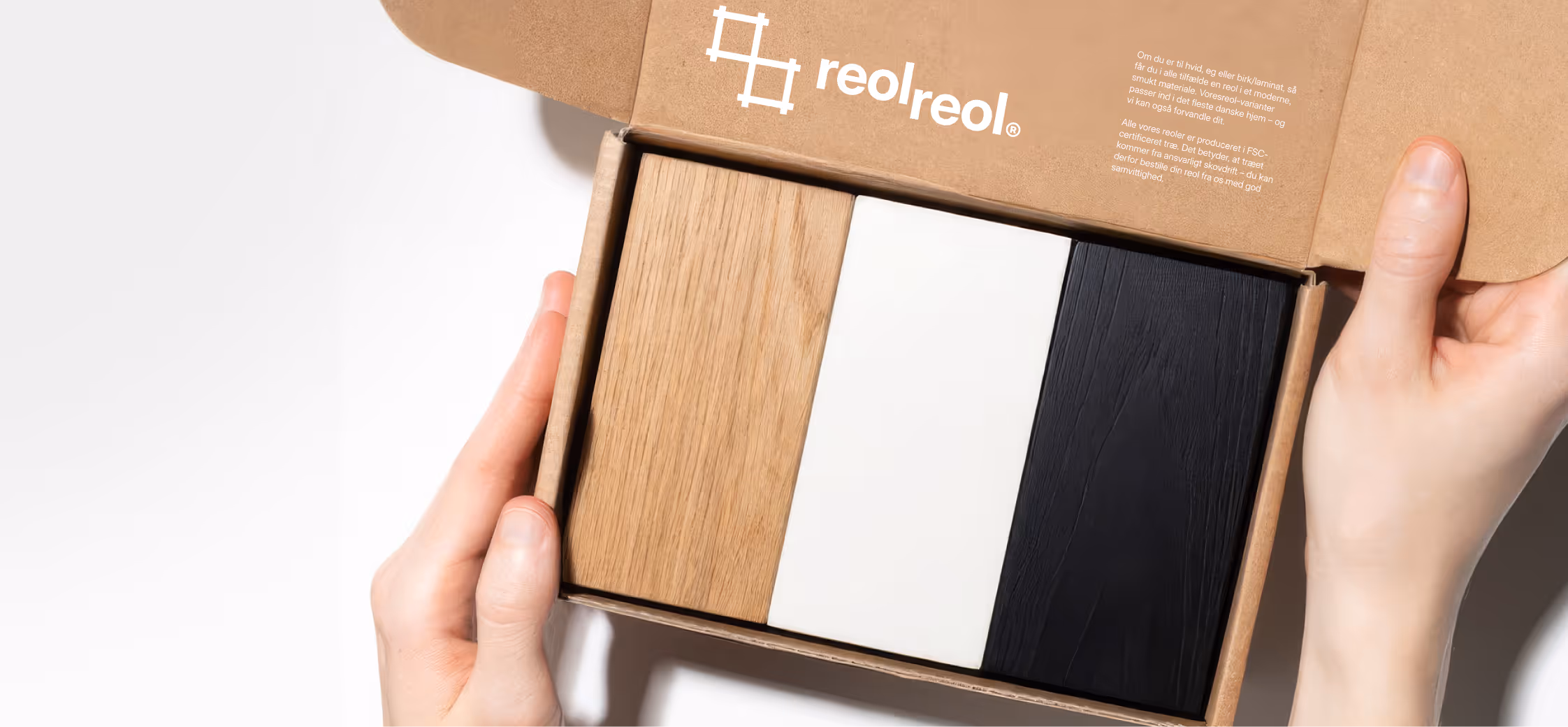 Hands holding an open box with three wood samples: natural, white, and black finishes.