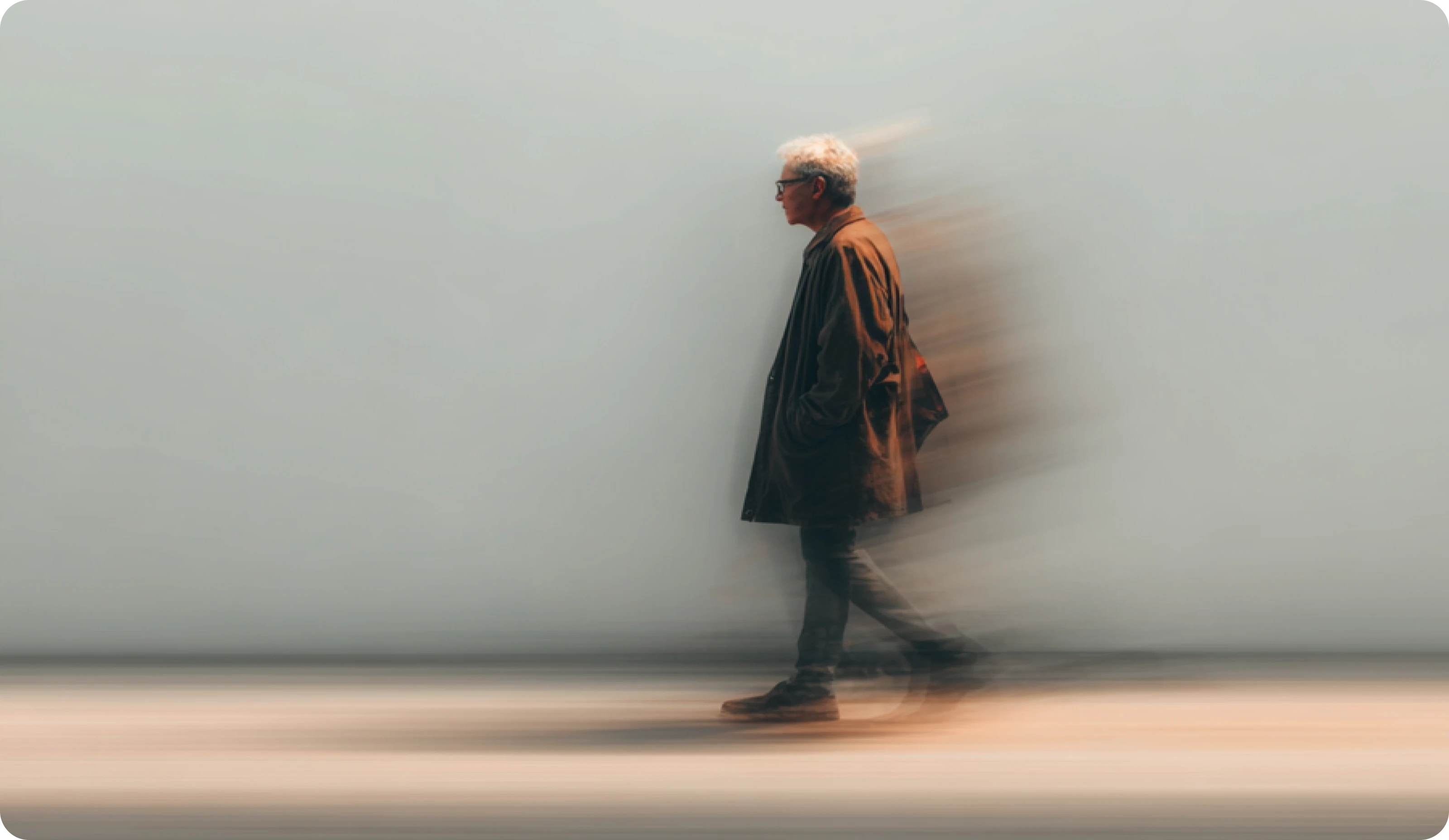 Man walking with motion blur effect and his hands in his coat pockets against a plain background.