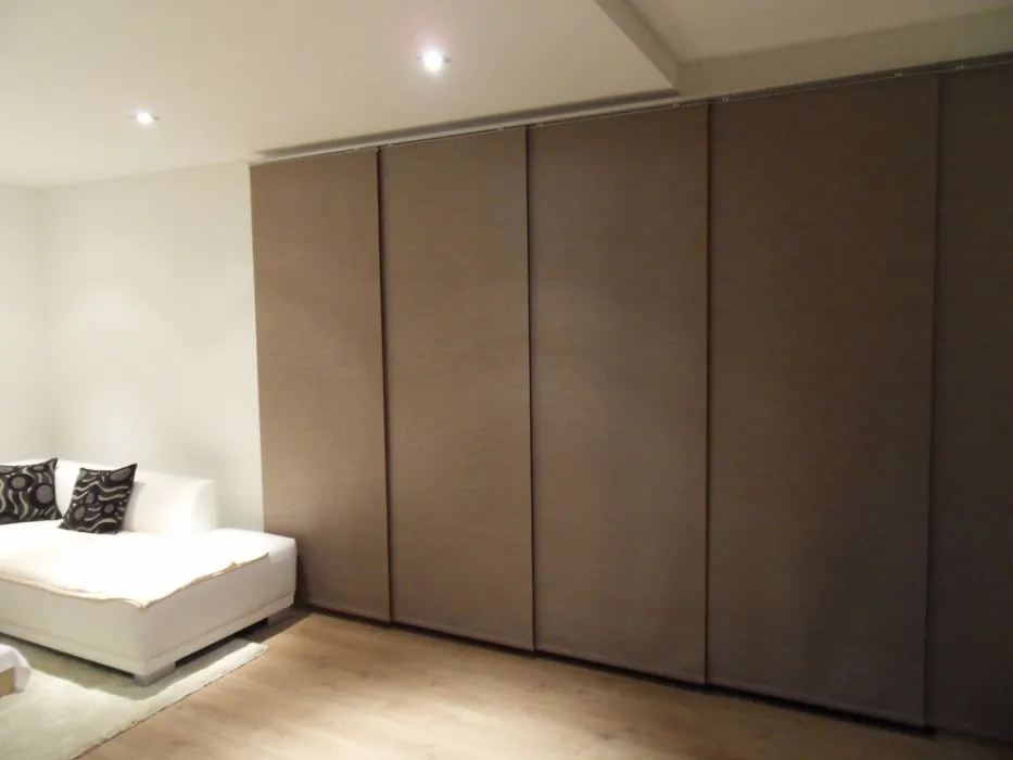 Modern room with white sofa and large brown fabric window blinds covering the wall.