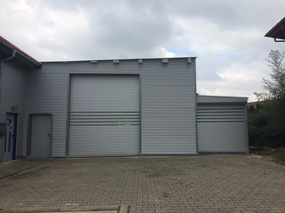 Modern commercial building with corrugated metal exterior and two large roll-up garage doors.
