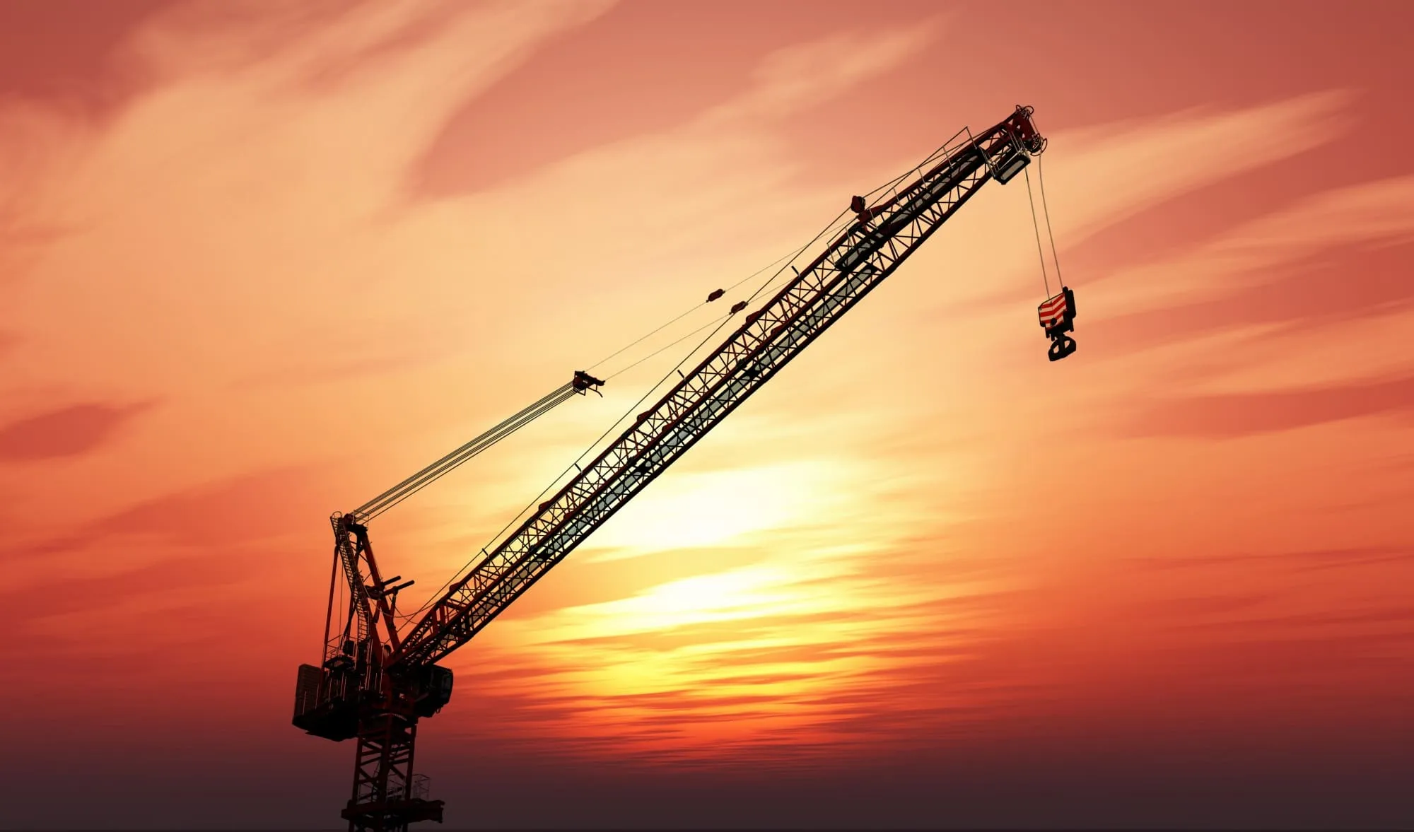 Construction crane silhouetted against an orange sunset sky with soft clouds.