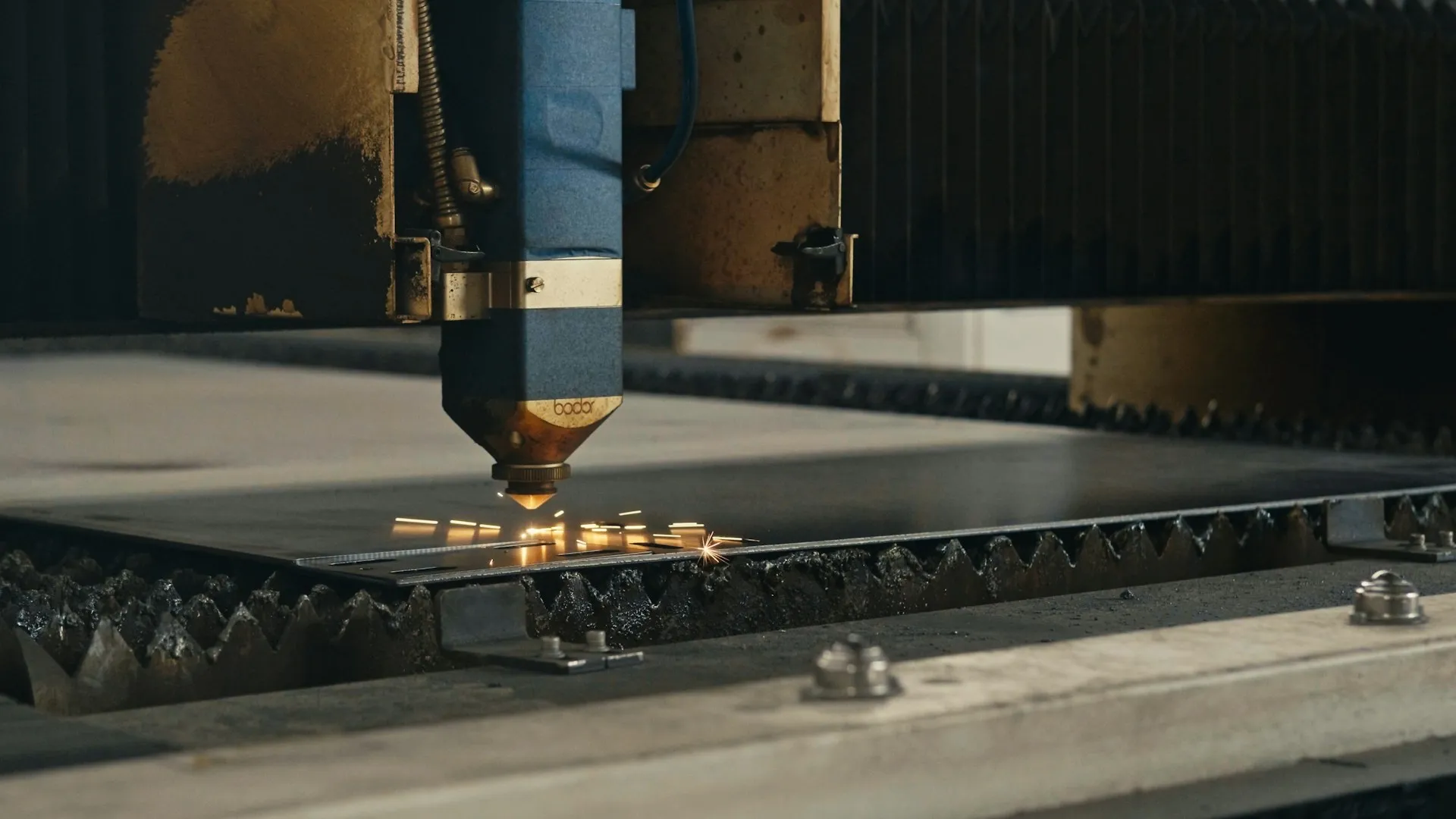 Laser cutting machine engraving sparks on a metal sheet in an industrial workshop.