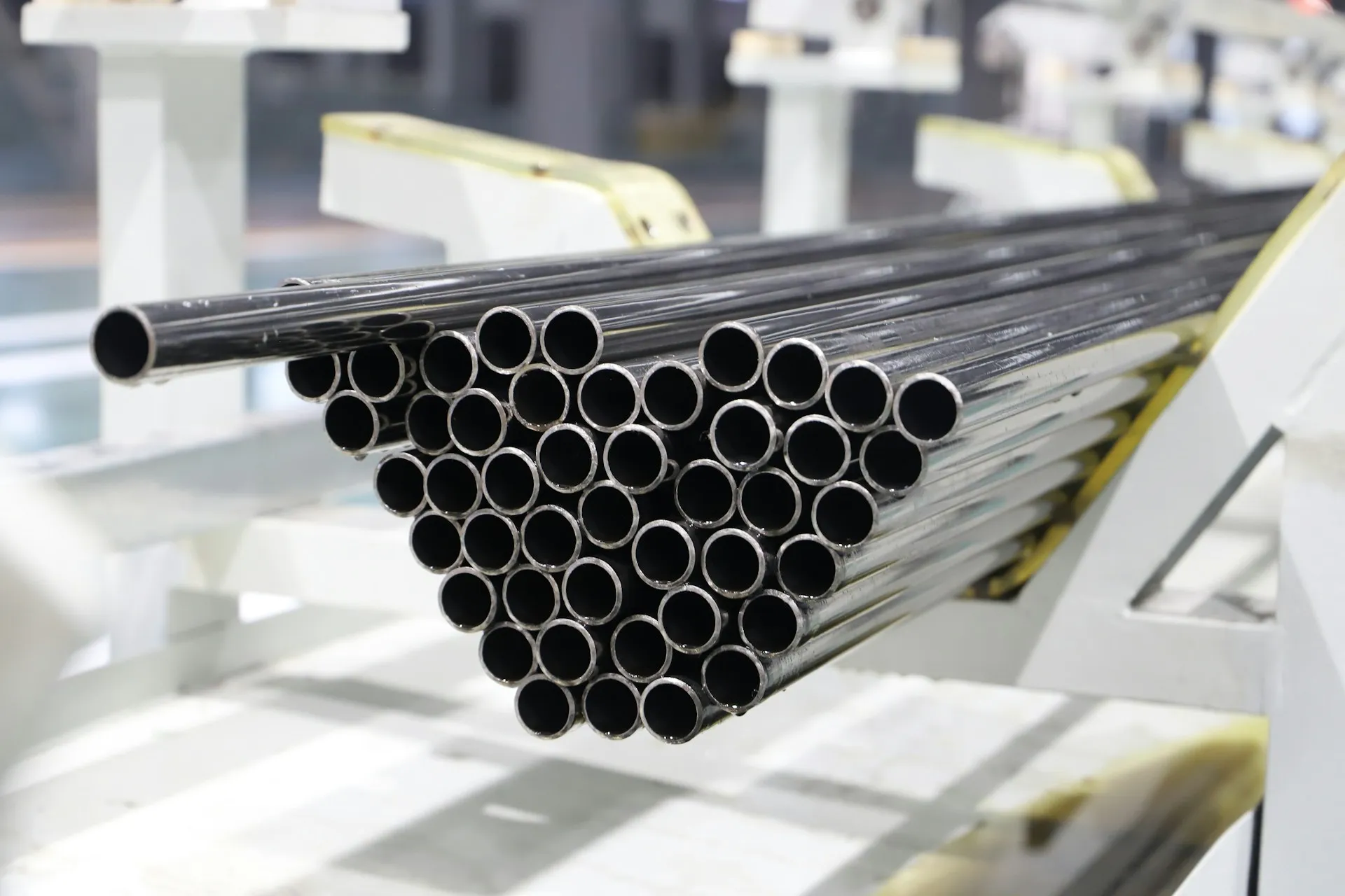 A bundle of shiny metal pipes arranged horizontally on a white industrial rack.