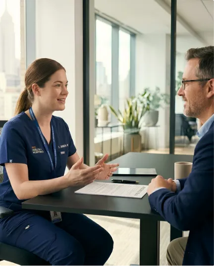 Healthcare professional in scrubs discussing paperwork with a man at an office table.