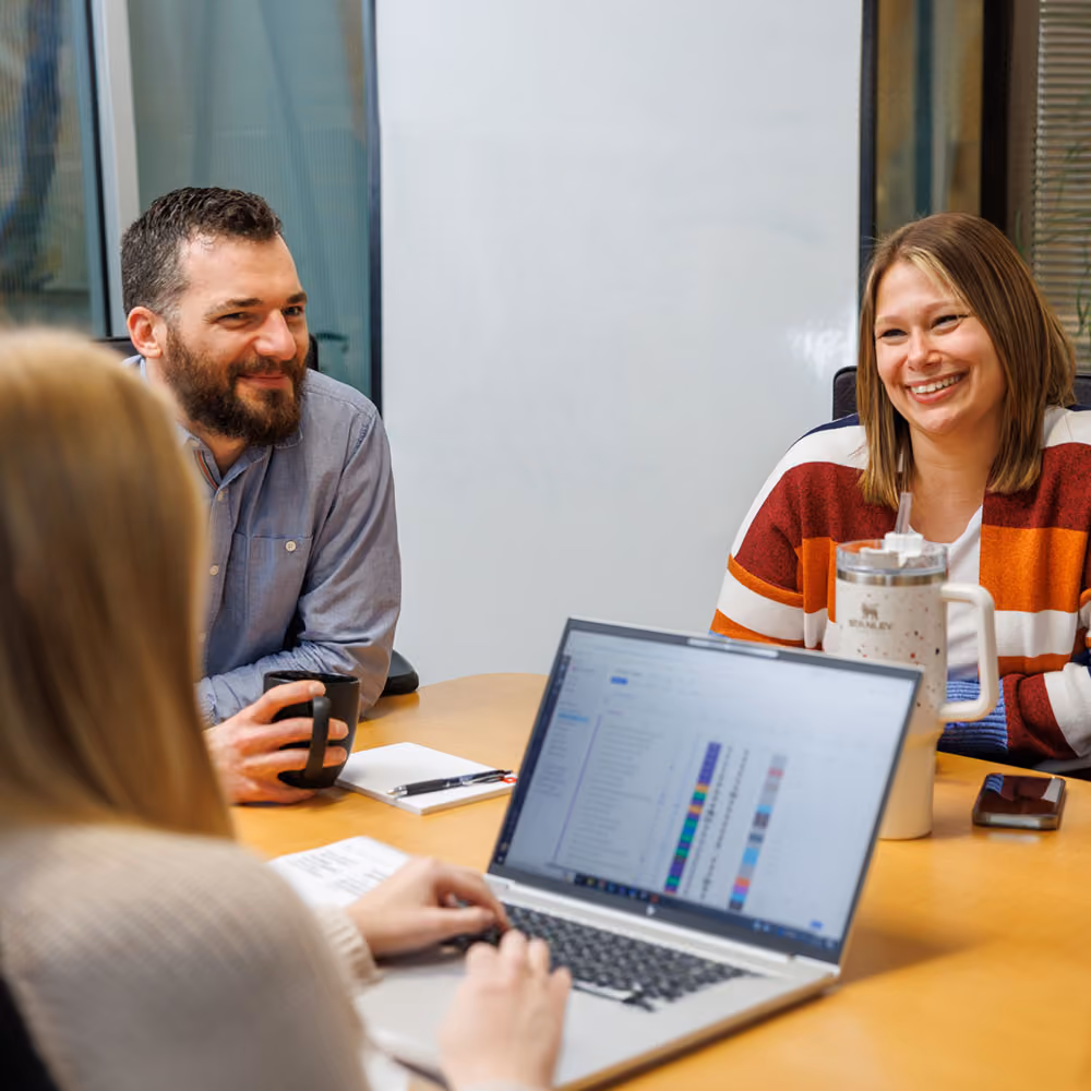 Three people at a conference table in an office having a discussion