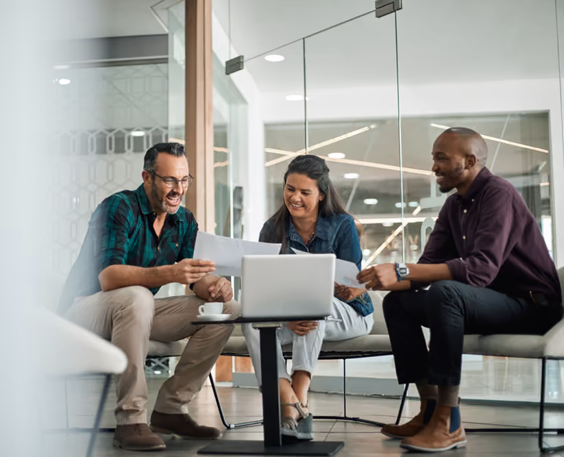 Two men and a women in a meeting space sitting around a computer