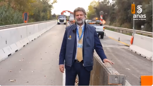 Uomo con badge davanti a un tratto stradale con barriere in calcestruzzo e un cartello ANAS
