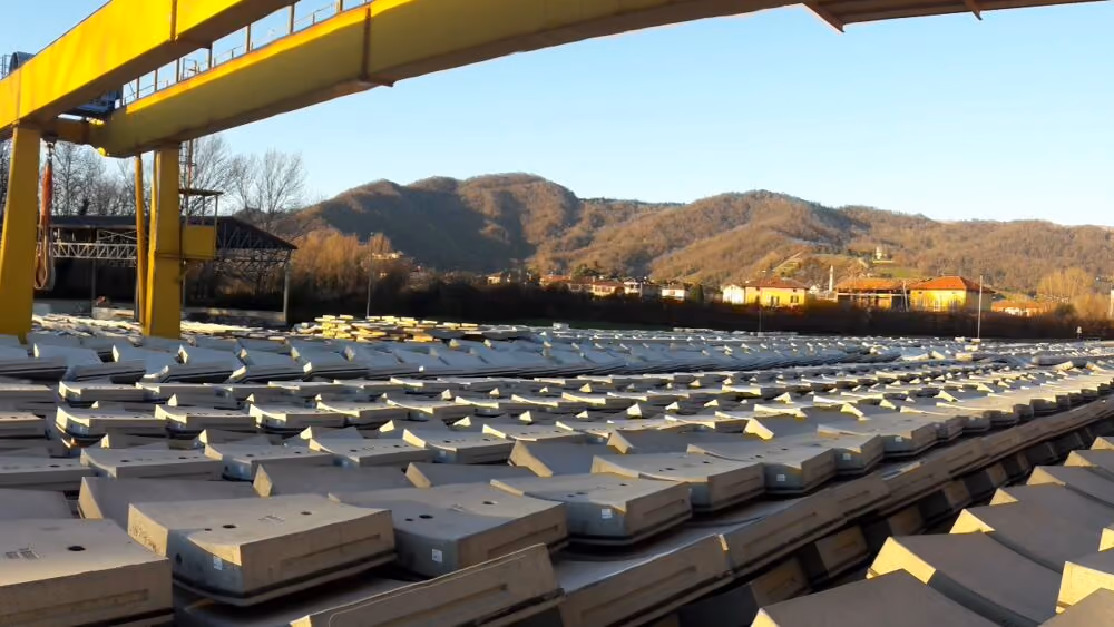 Carroponte giallo sopra file di elementi prefabbricati, con le colline sullo sfondo