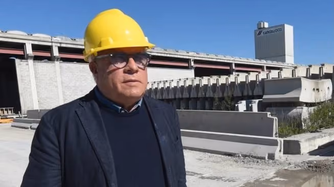 Uomo con casco giallo e giacca scura davanti a elementi prefabbricati in calcestruzzo