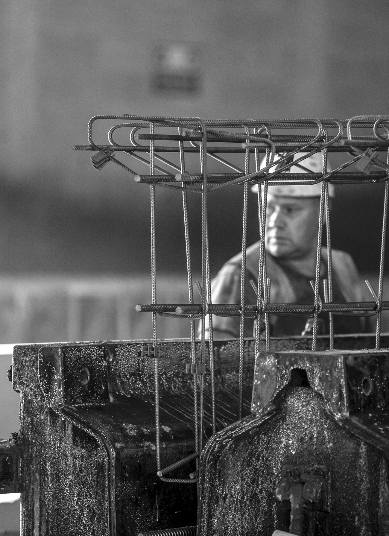 Operaio con casco dietro una gabbia di armatura in ferro, in bianco e nero