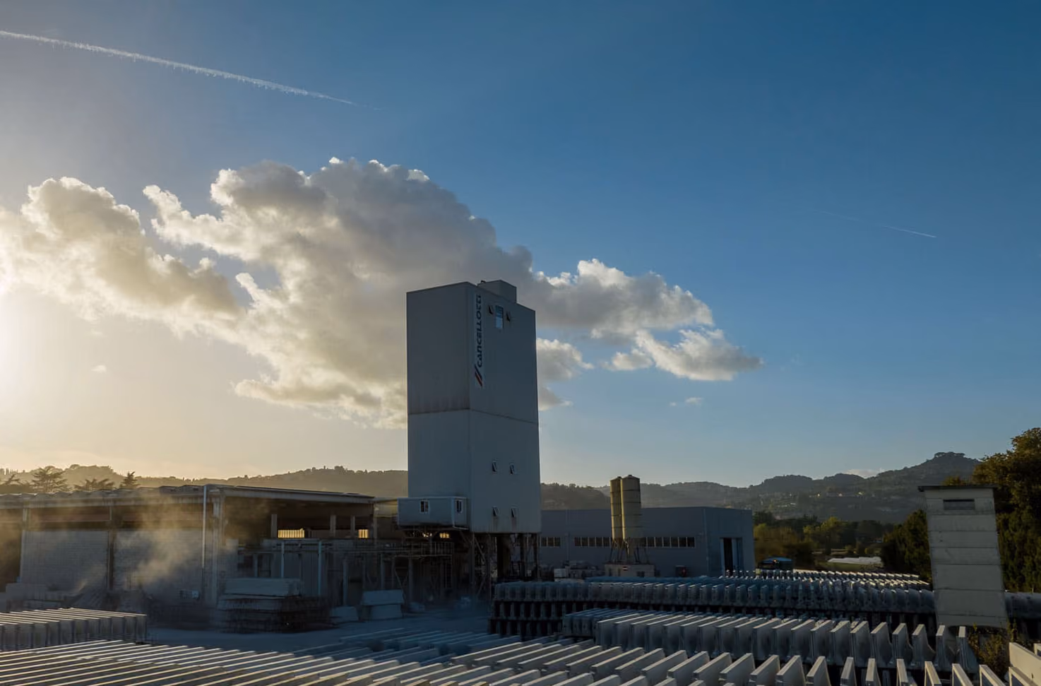 Impianto di produzione con silo al tramonto, sotto un cielo con nuvole