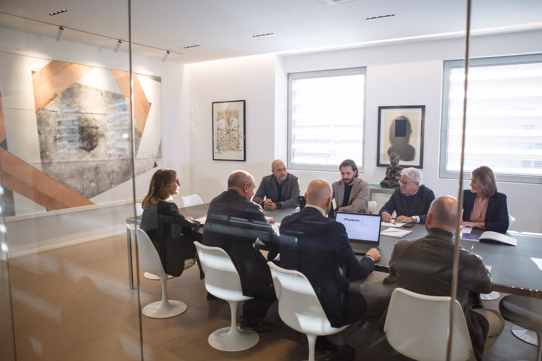 Riunione di lavoro attorno a un tavolo, in una sala con opere d'arte alle pareti
