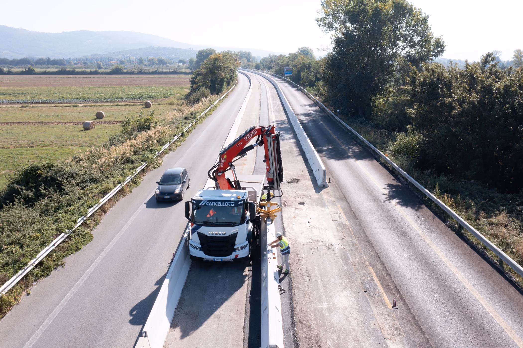 Camion con gru che posiziona barriere in calcestruzzo su una strada di campagna