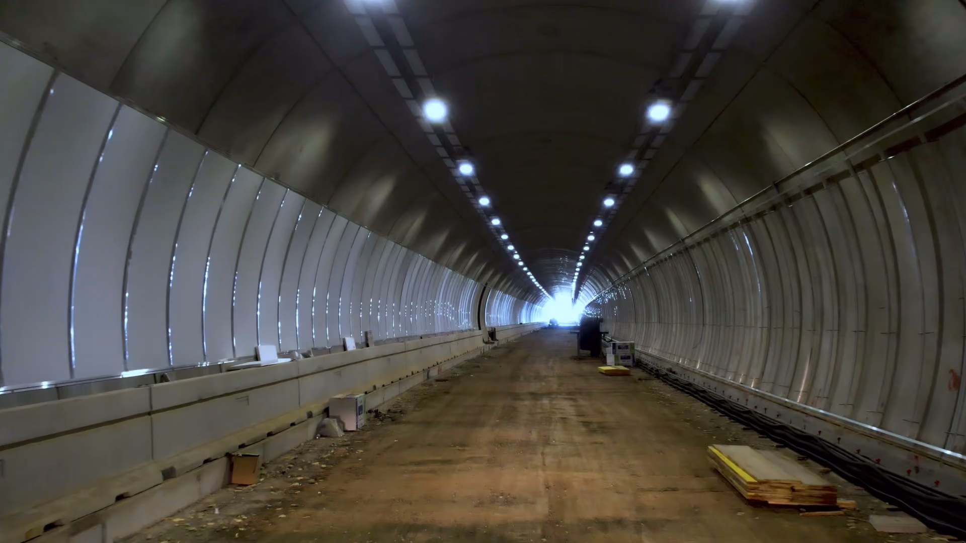 Galleria in costruzione con rivestimento a pannelli e luci accese lungo la volta