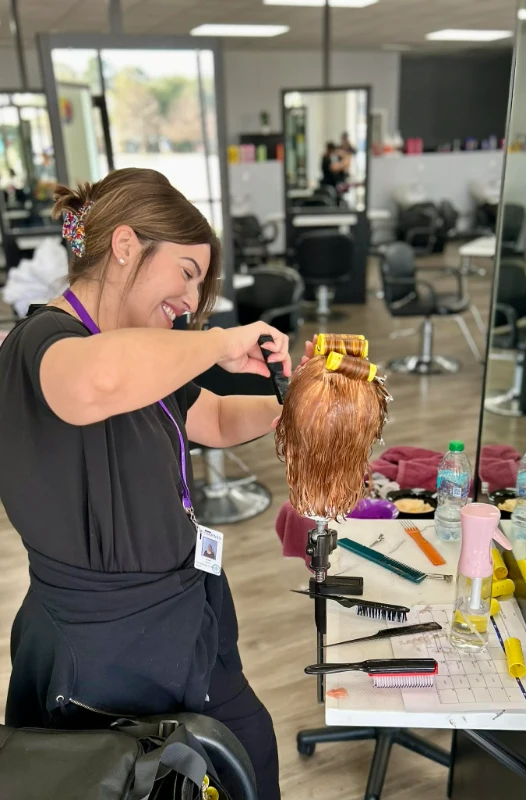 Compass Career College Cosmetology student with hair clips styling a mannequin head with curlers in a hair salon training setting.
