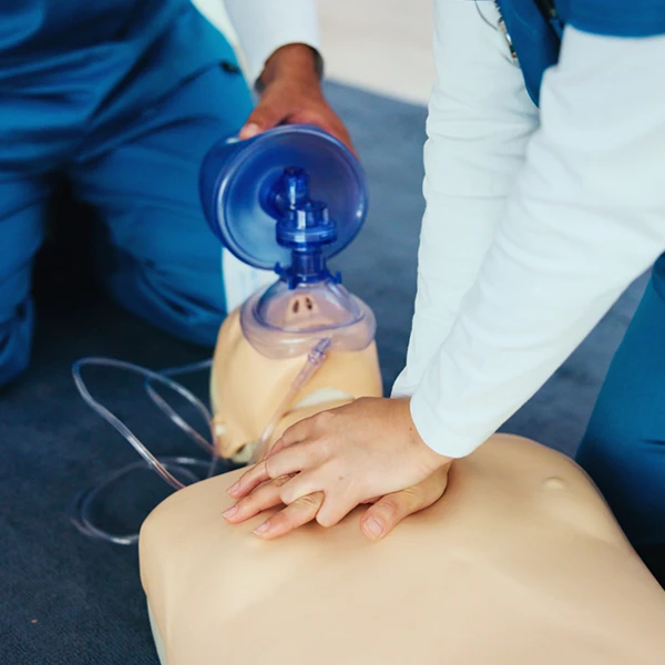 Compass Career College students performing CPR chest compressions and ventilation on a training manikin.