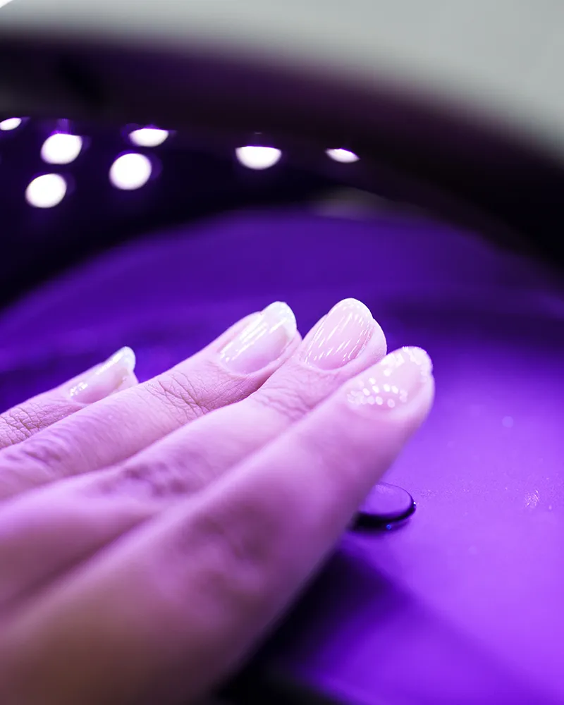 Hand with freshly cured shiny nails under a purple UV light dryer at Compass Career College