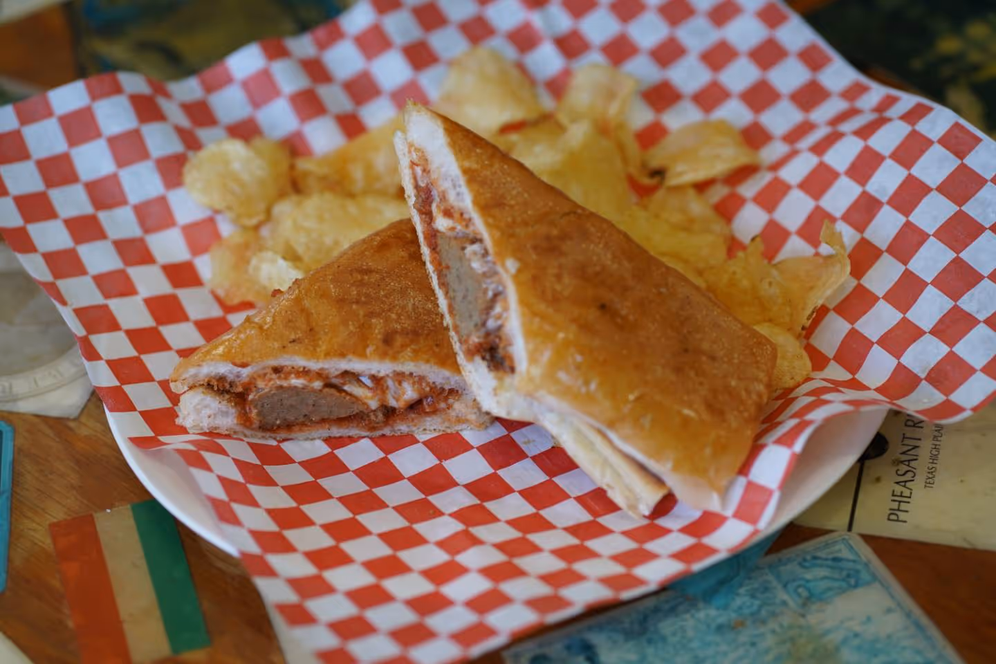 Meatball sandwich on toasted bread served with potato chips on red and white checkered paper.