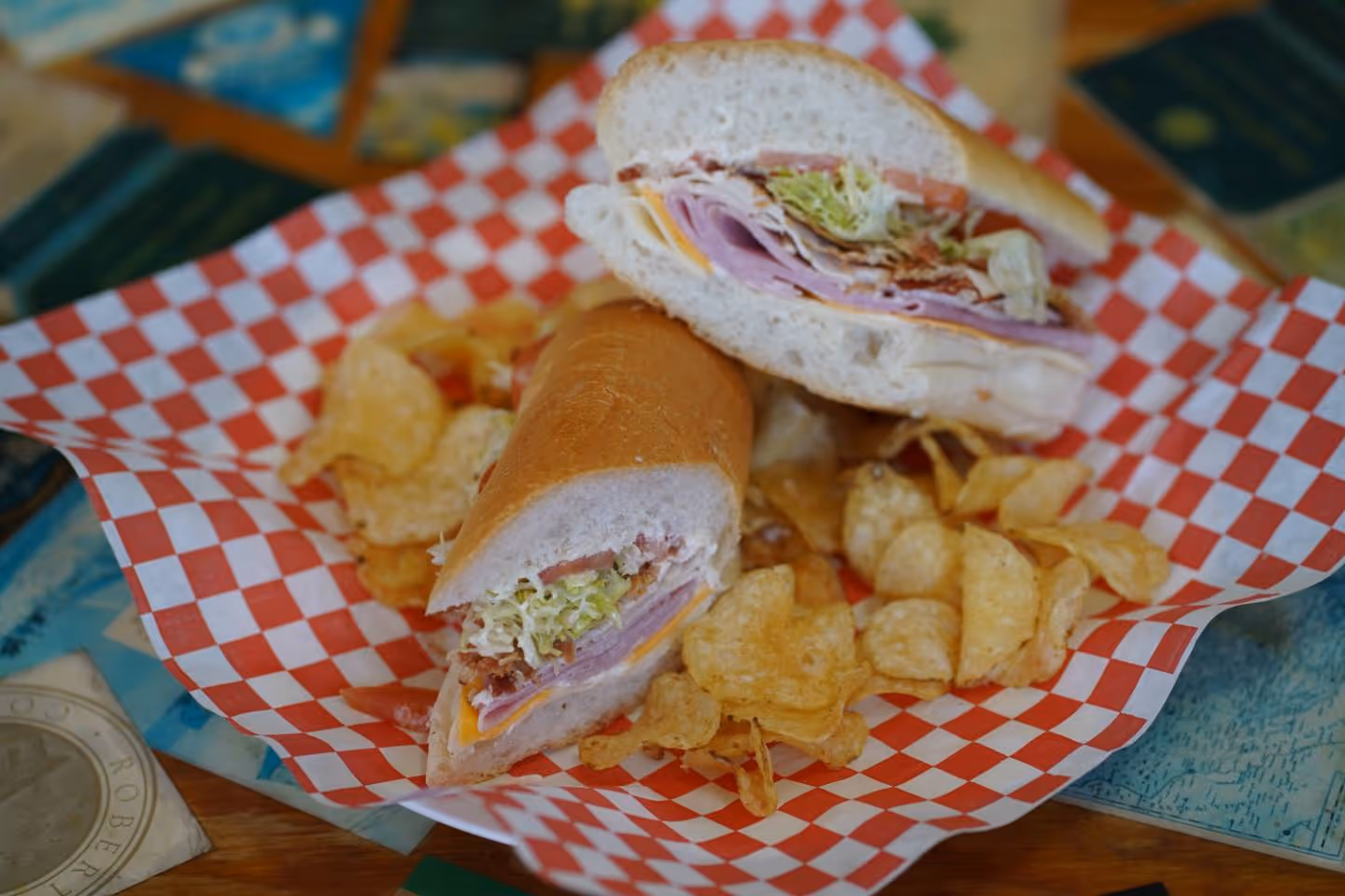 Ham and turkey sandwich with lettuce, tomato, and bacon on white sub bread with potato chips.