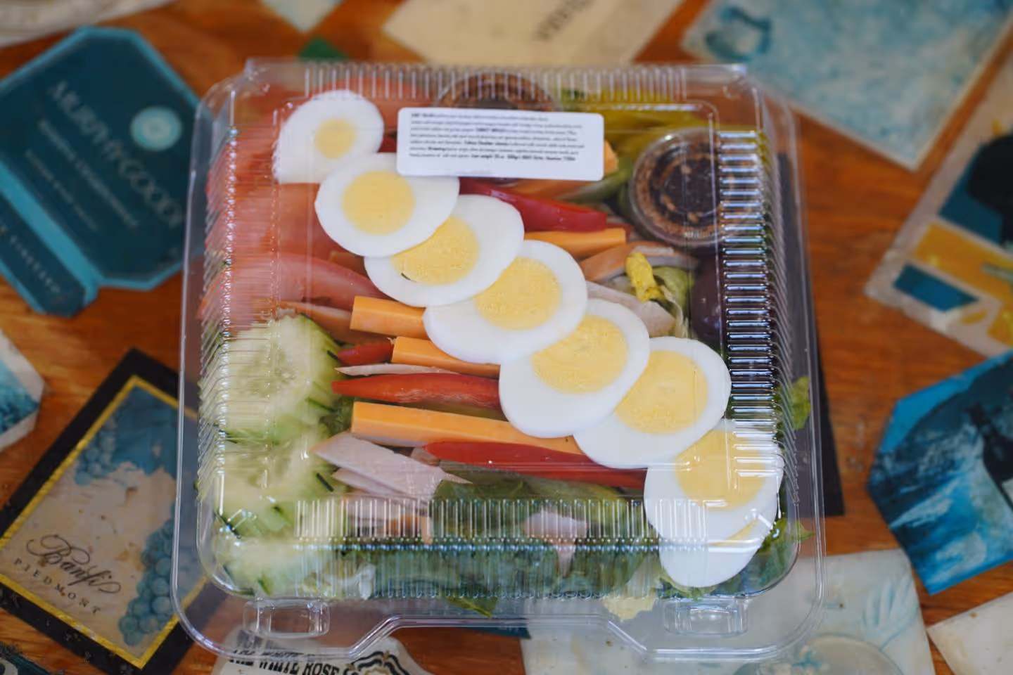 Salad with sliced hard-boiled eggs, cucumber, tomato, red pepper, and turkey in plastic container.