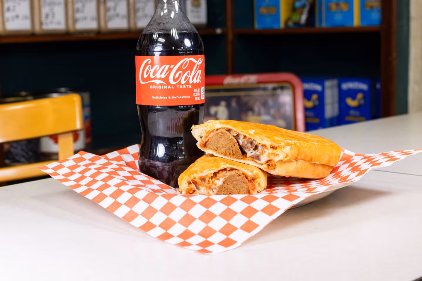 Bottle of Coca-Cola and sandwich with meatball and melted cheese on checkered paper.