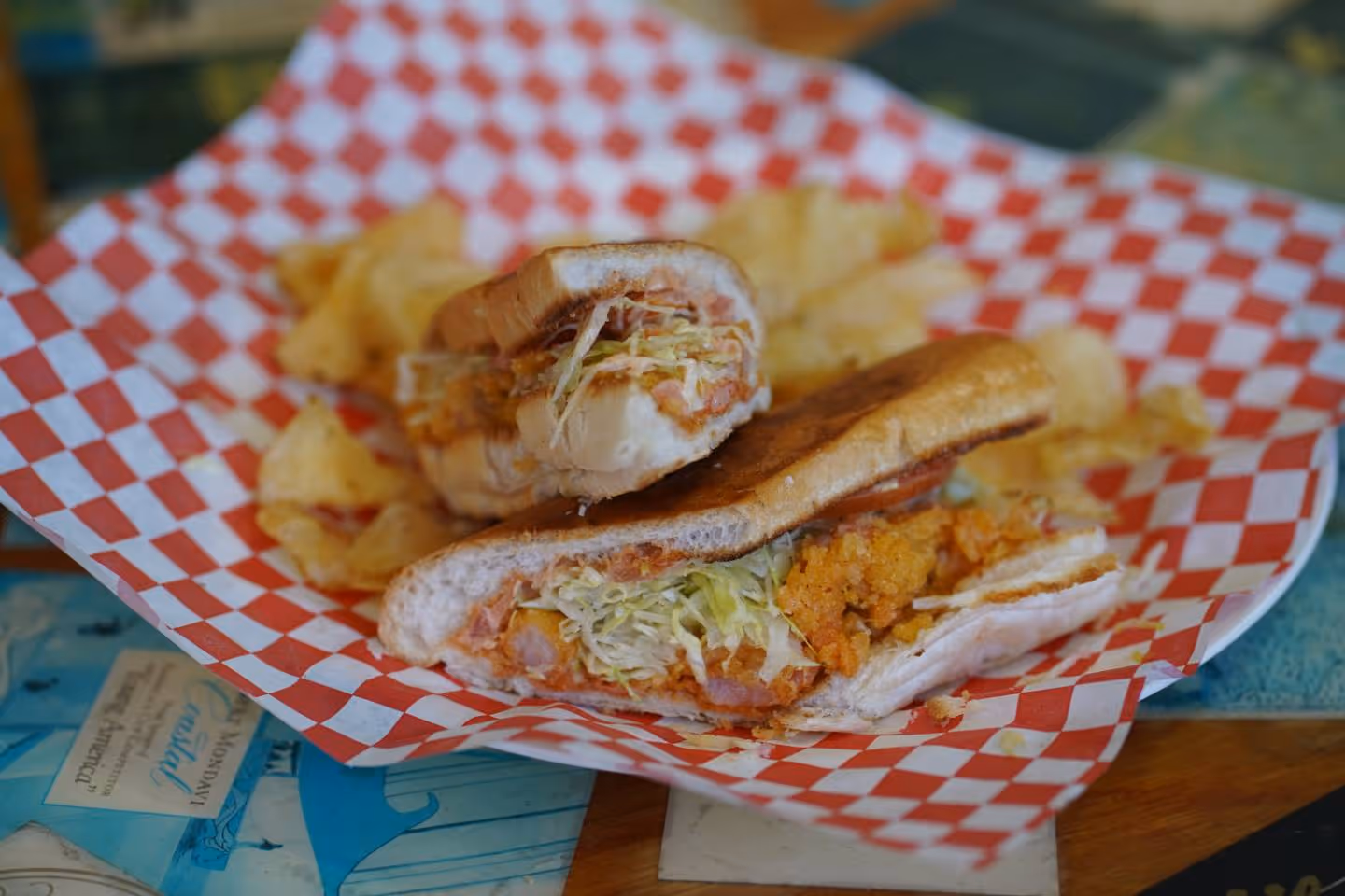 Fried shrimp po'boy sandwich with lettuce served with potato chips on checkered paper.