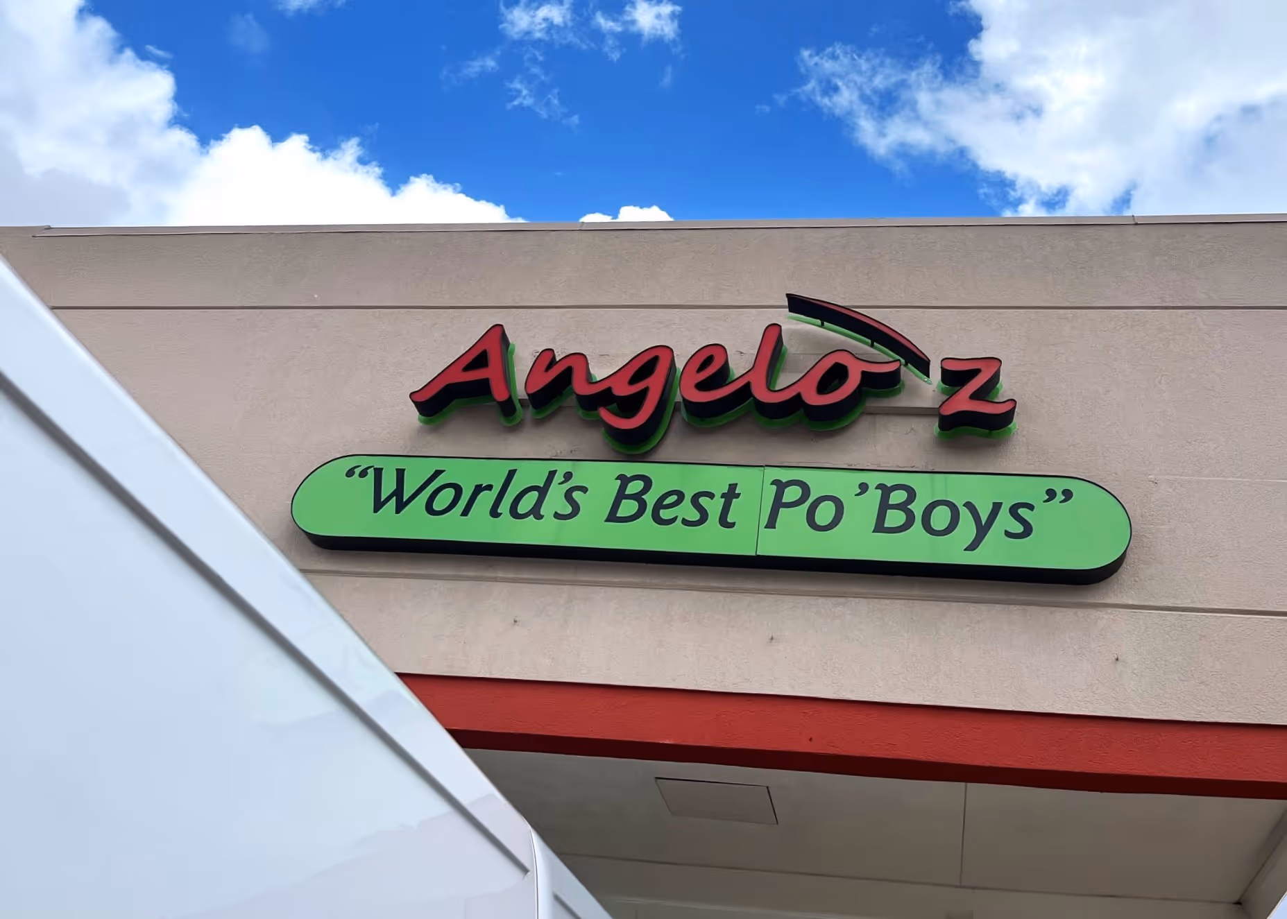 Angelo'z restaurant sign reading 'World's Best Po' Boys' under blue sky with clouds.
