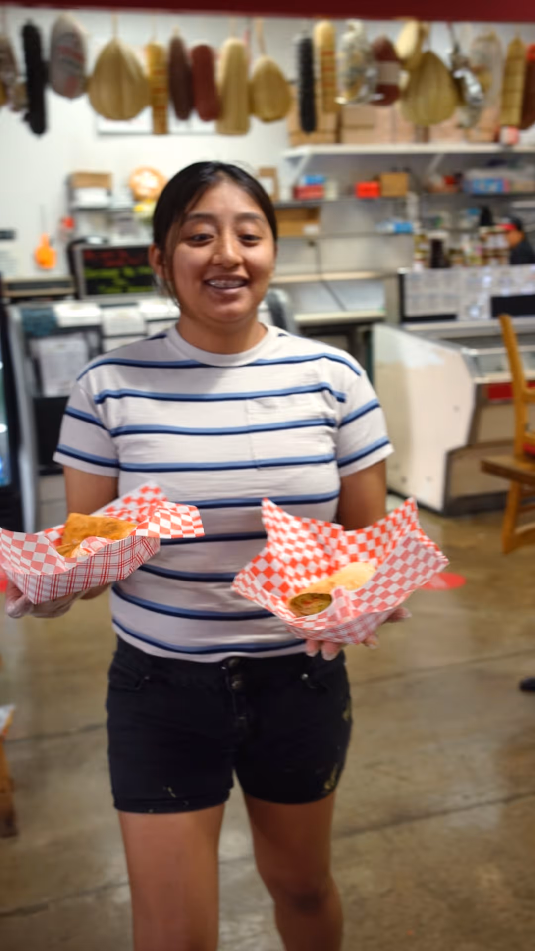 Woman in striped shirt holding two baskets with wrapped food inside a store or deli.