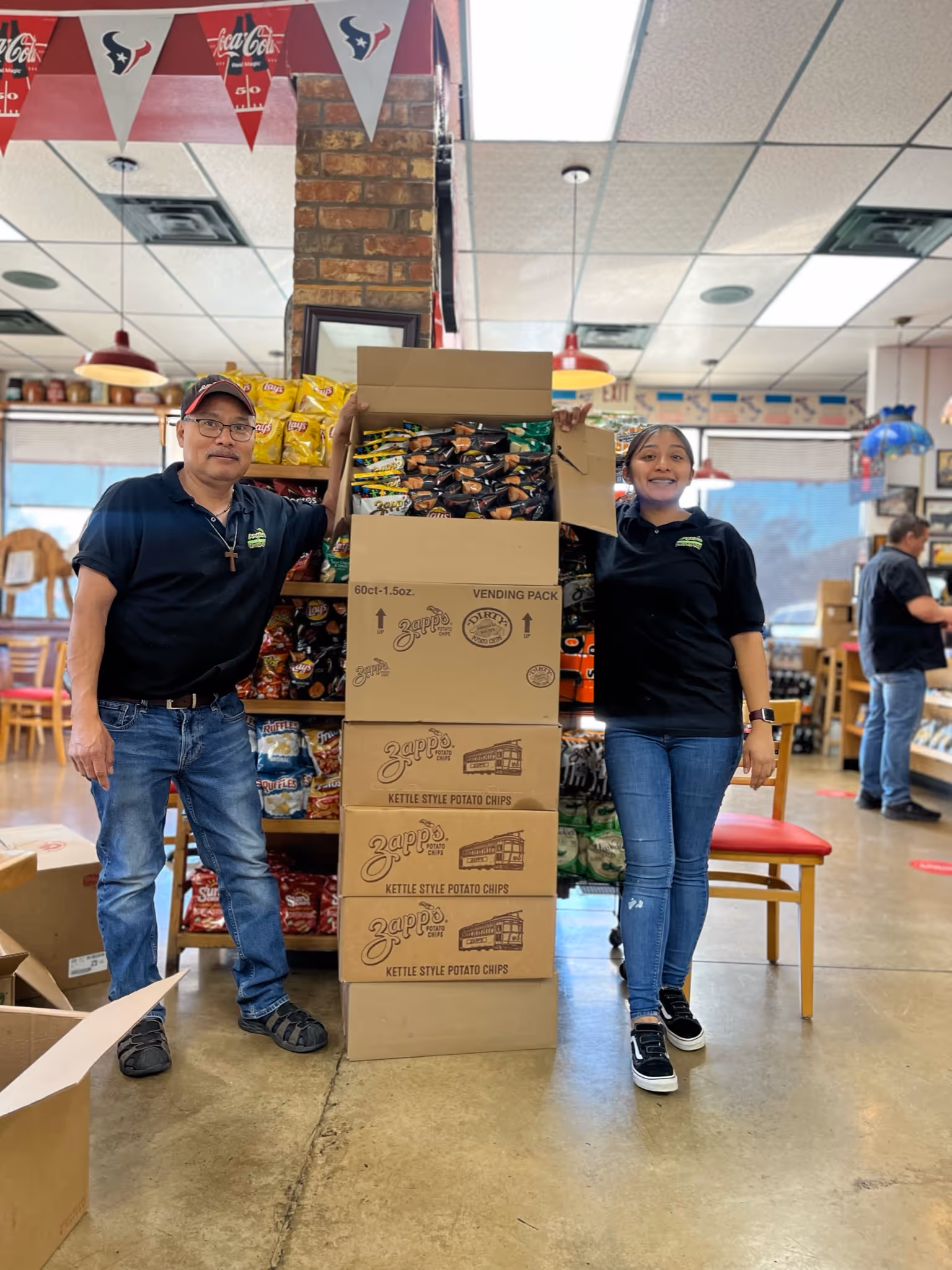 Man and woman standing next to stacked Zapp's kettle style potato chips boxes inside a store.